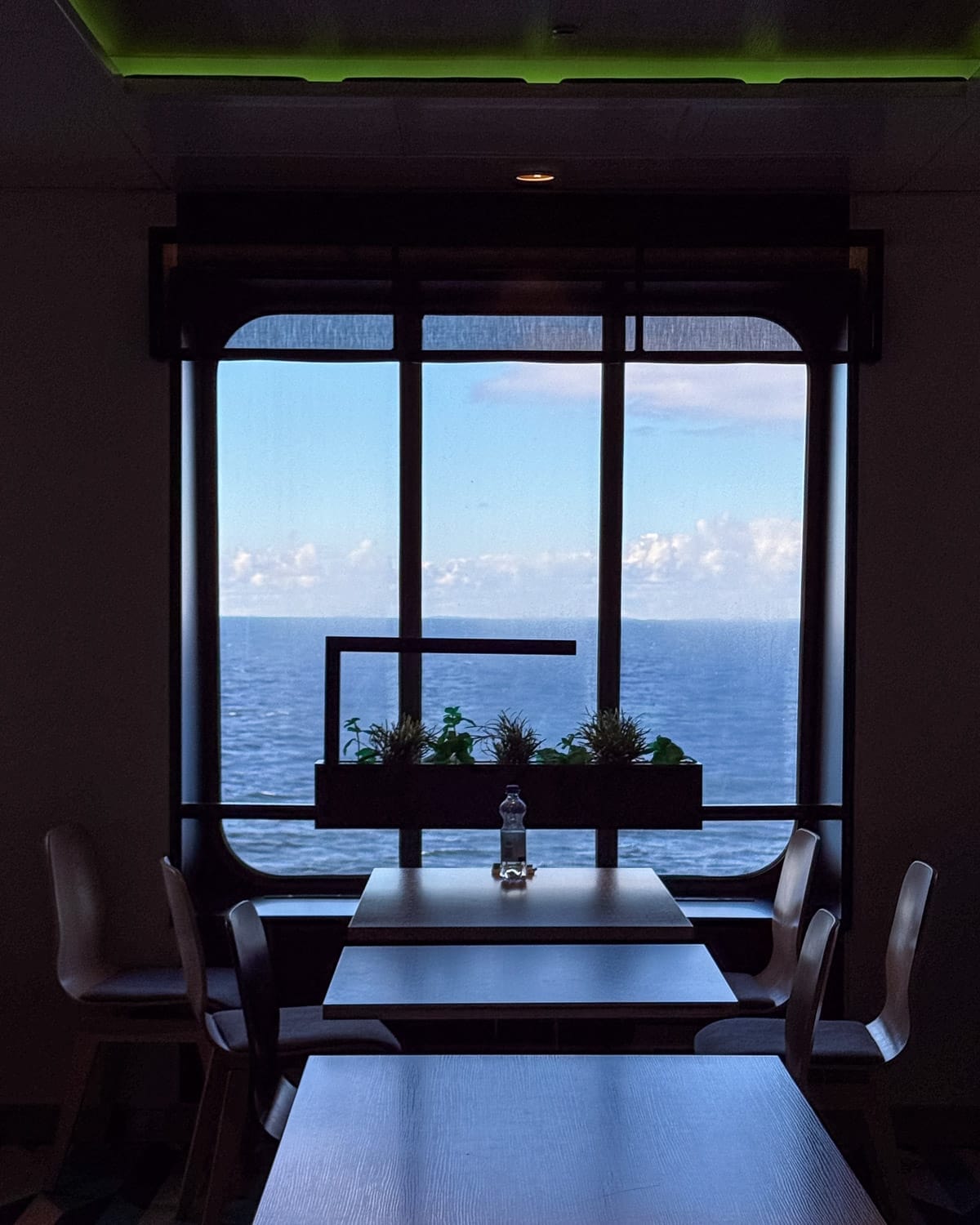 Minimalist ferry cafe interior on Tallink Silja ferry with tables and chairs facing a large window overlooking the open Baltic Sea, soft blue sky and horizon visible beyond.