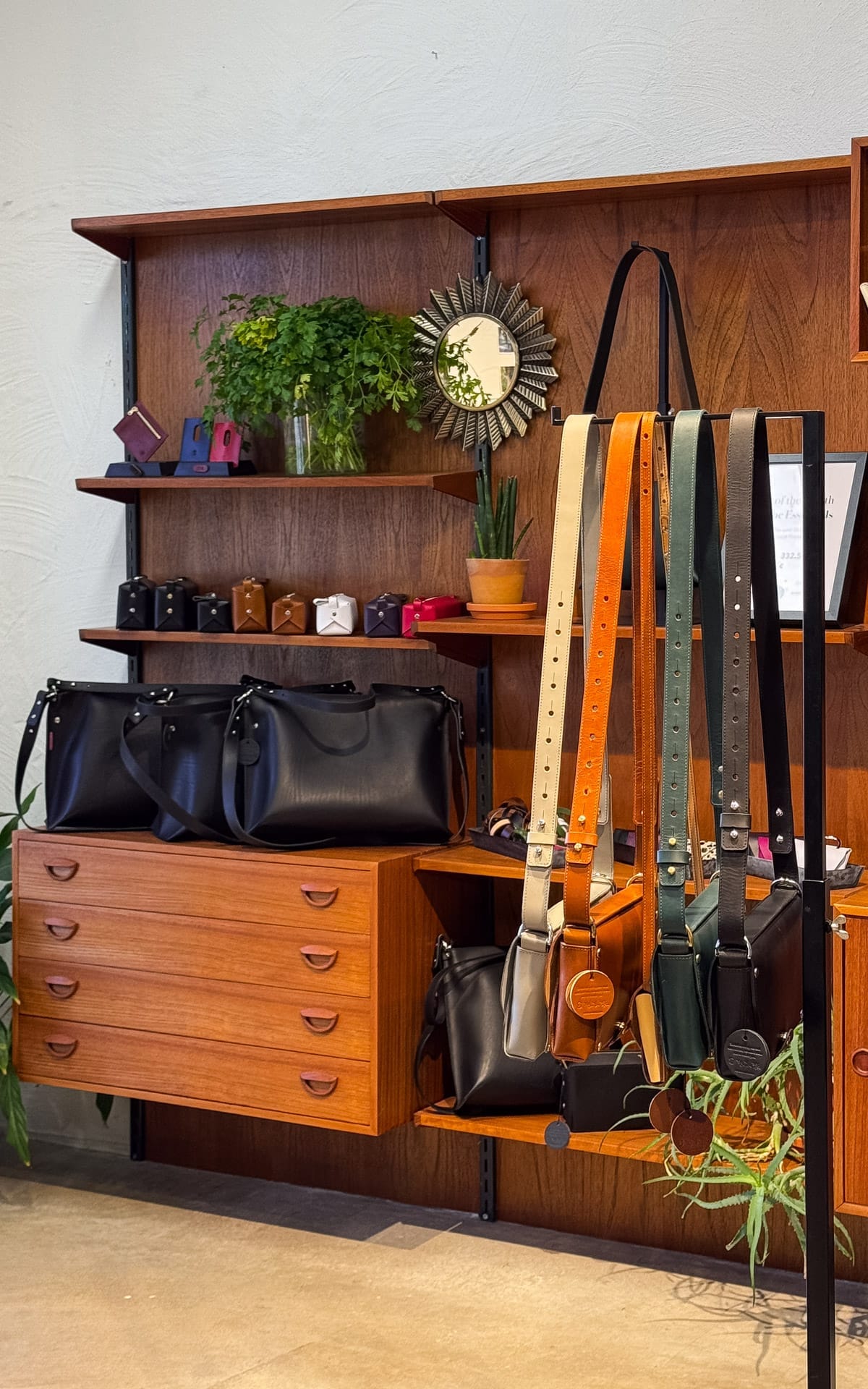 Display of handmade leather bags on mid-century wooden shelving inside Stella Soomlais design boutique.
