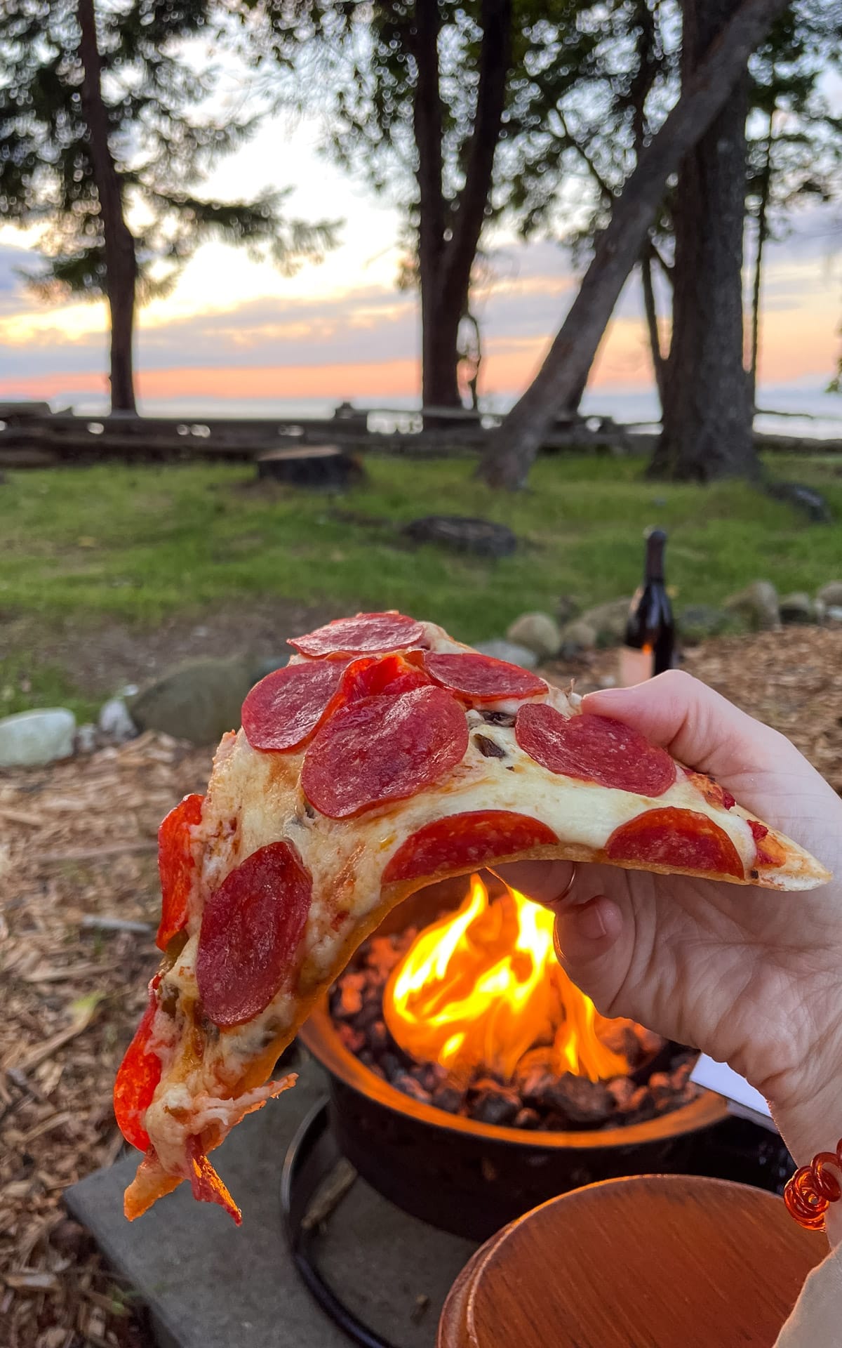 Slice of pepperoni pizza enjoyed by a fire pit overlooking the ocean on Hornby Island. 
