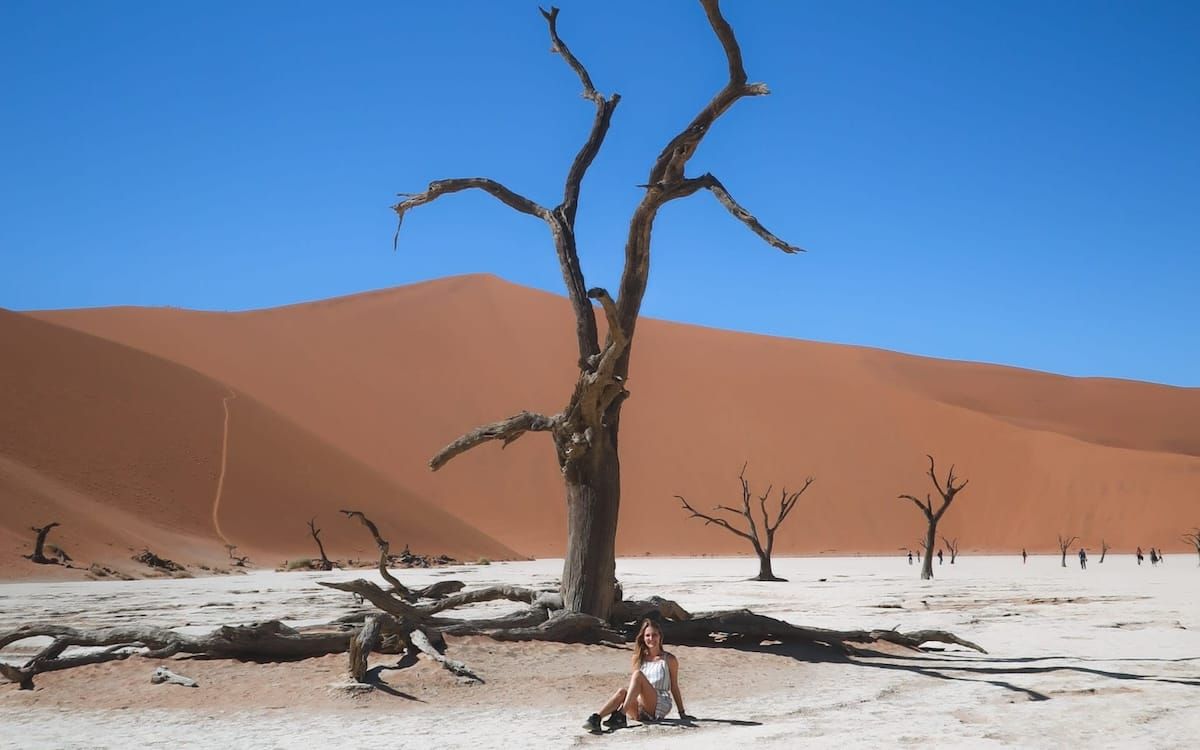 Cec sits under a camel thorn tree amid towering red dunes in Deadvlei, Namibia, one of Africa’s best travel destinations.