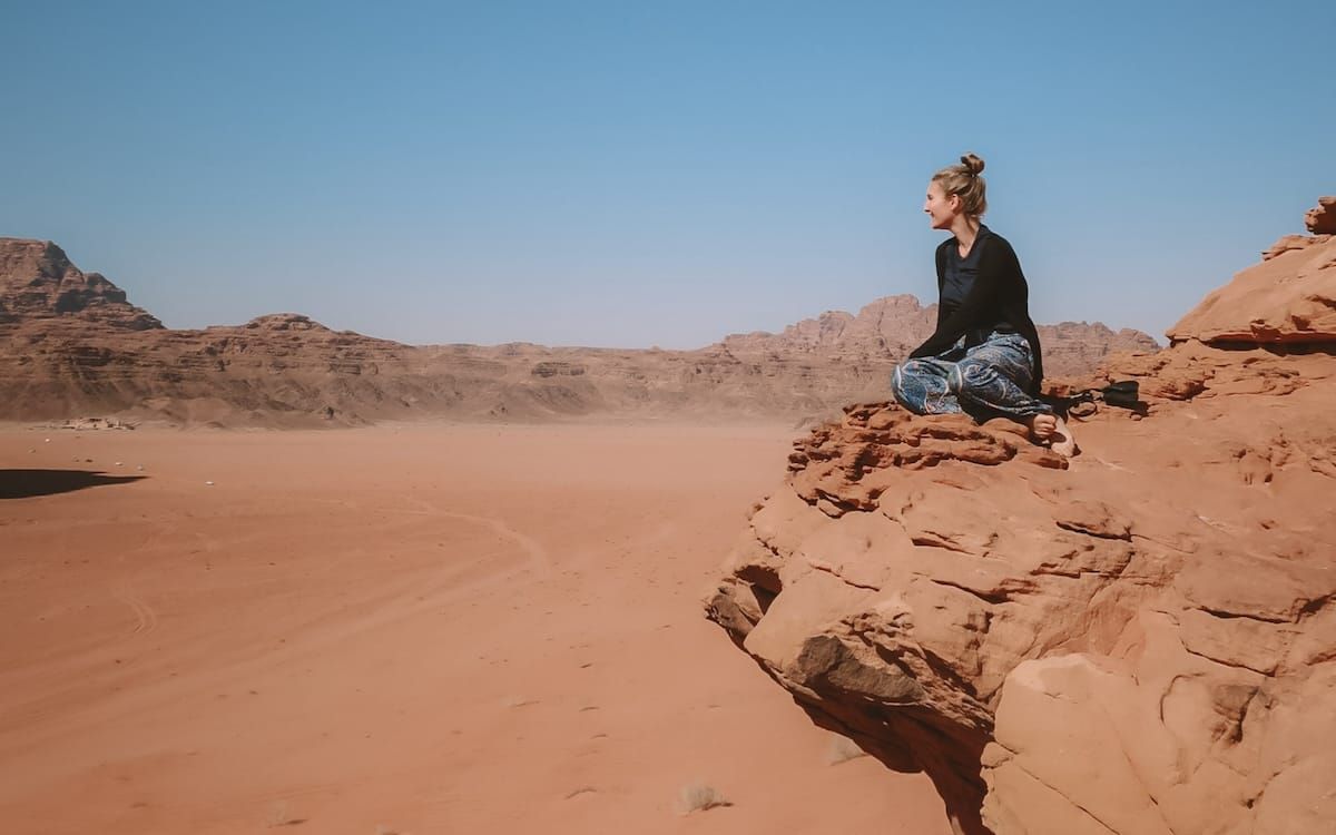 Cec sits on a cliff overlooking the vast Wadi Rum Desert in Jordan, one of the most amazing travel destinations in the Middle East.