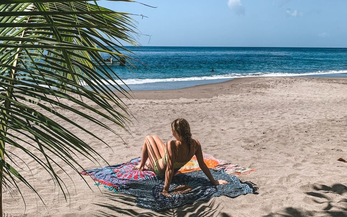 Cec lounges on a colourful beach blanket under palm fronds in St. Lucia, a relaxing travel destination.