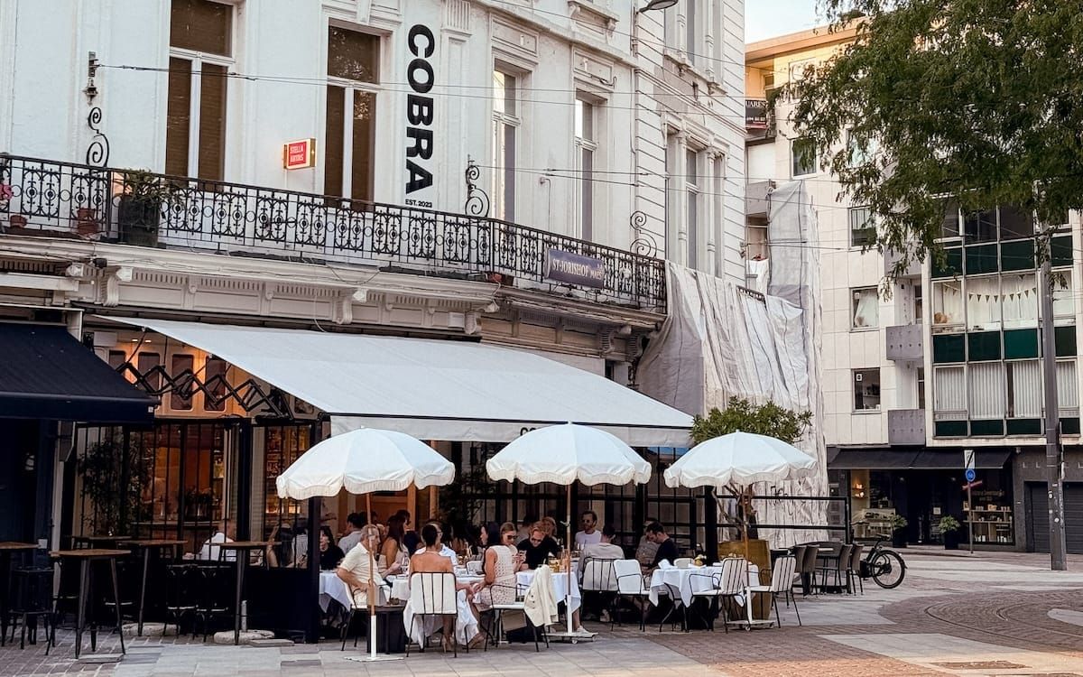 Diners sit under white umbrellas outside Cobra restaurant, a top dining spot featured in this Antwerp itinerary.