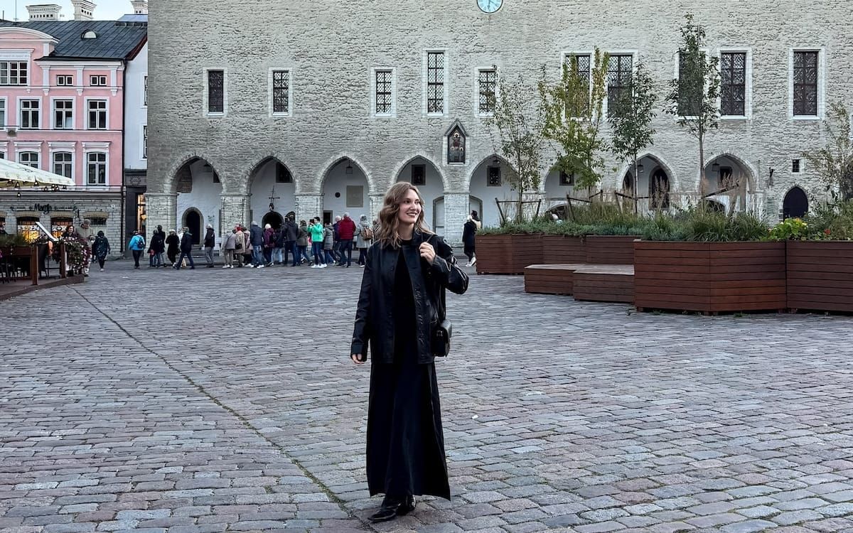Cec walking across cobblestones in Tallinn’s Old Town with medieval stone arches and pastel buildings in the background.