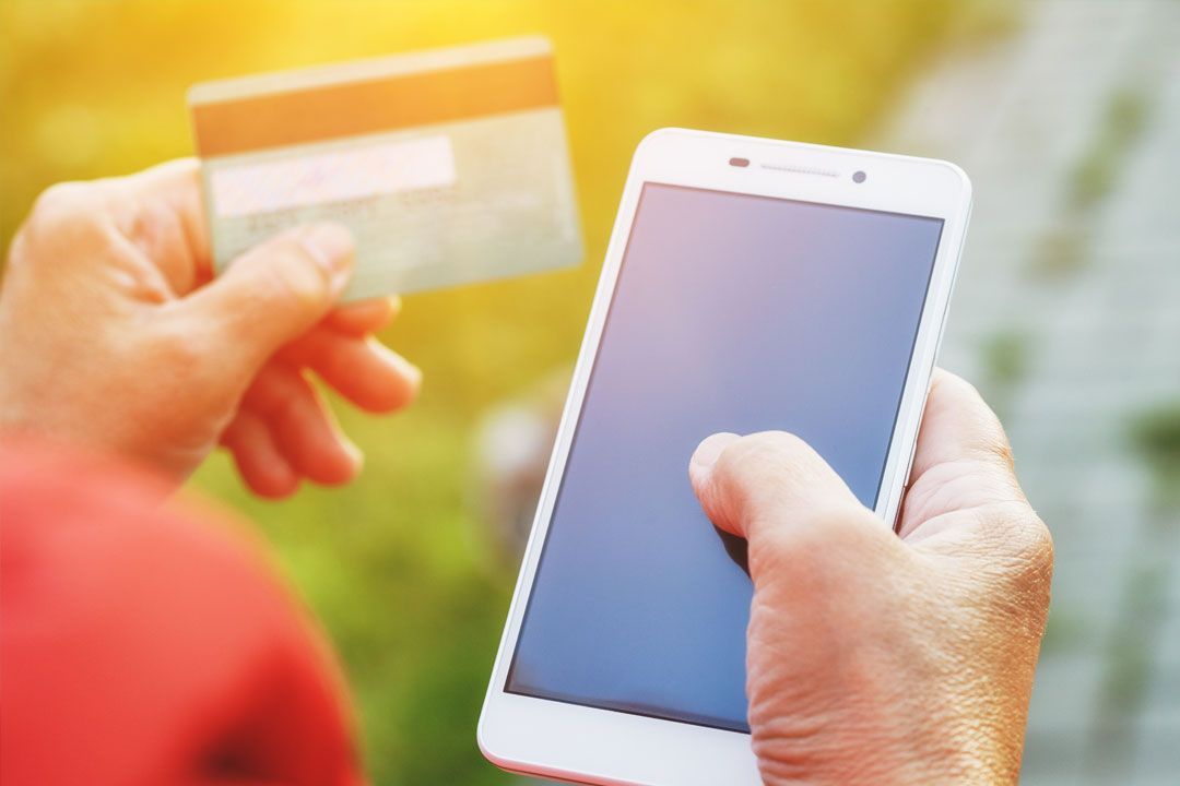 Image of woman's hands holding a mobile phone and entering credit card details.