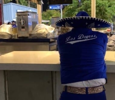 A man sits at a bar with a blue sombrero and blue jacket that says "Los Doyers" across the back.