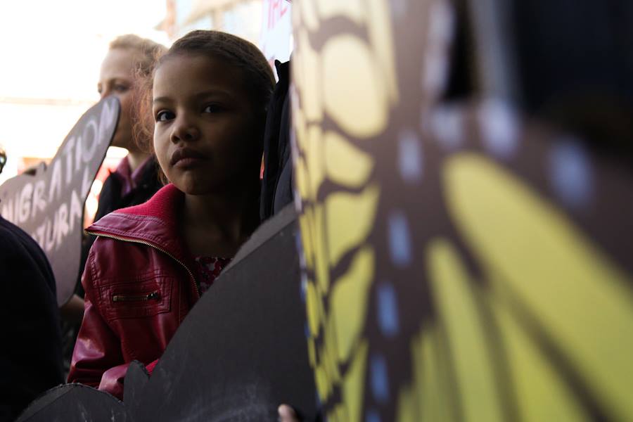A girl stands beside a butterfly cutout with a sign behind her reading 'Migration'