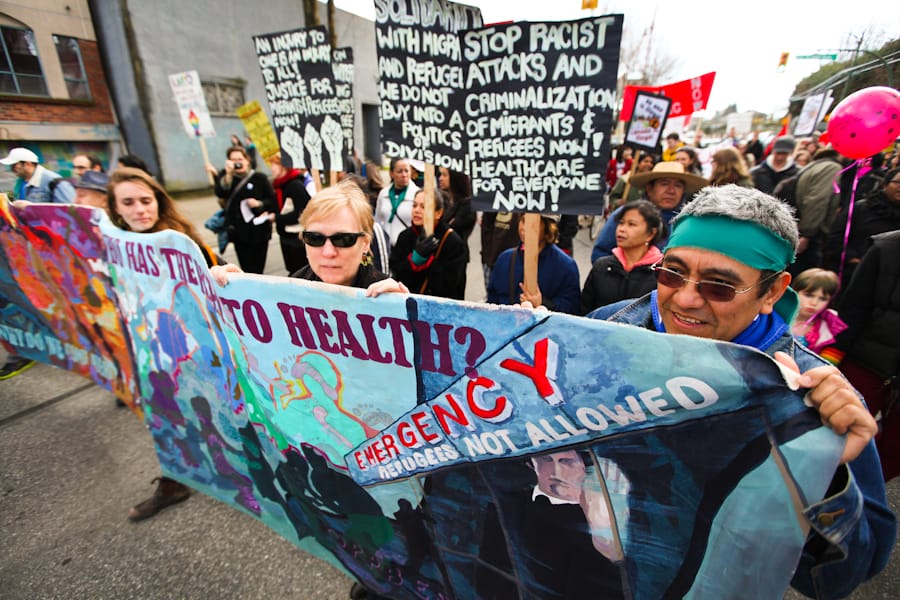 People march behind a banner reading "Health, emergency: refugees not allowed"