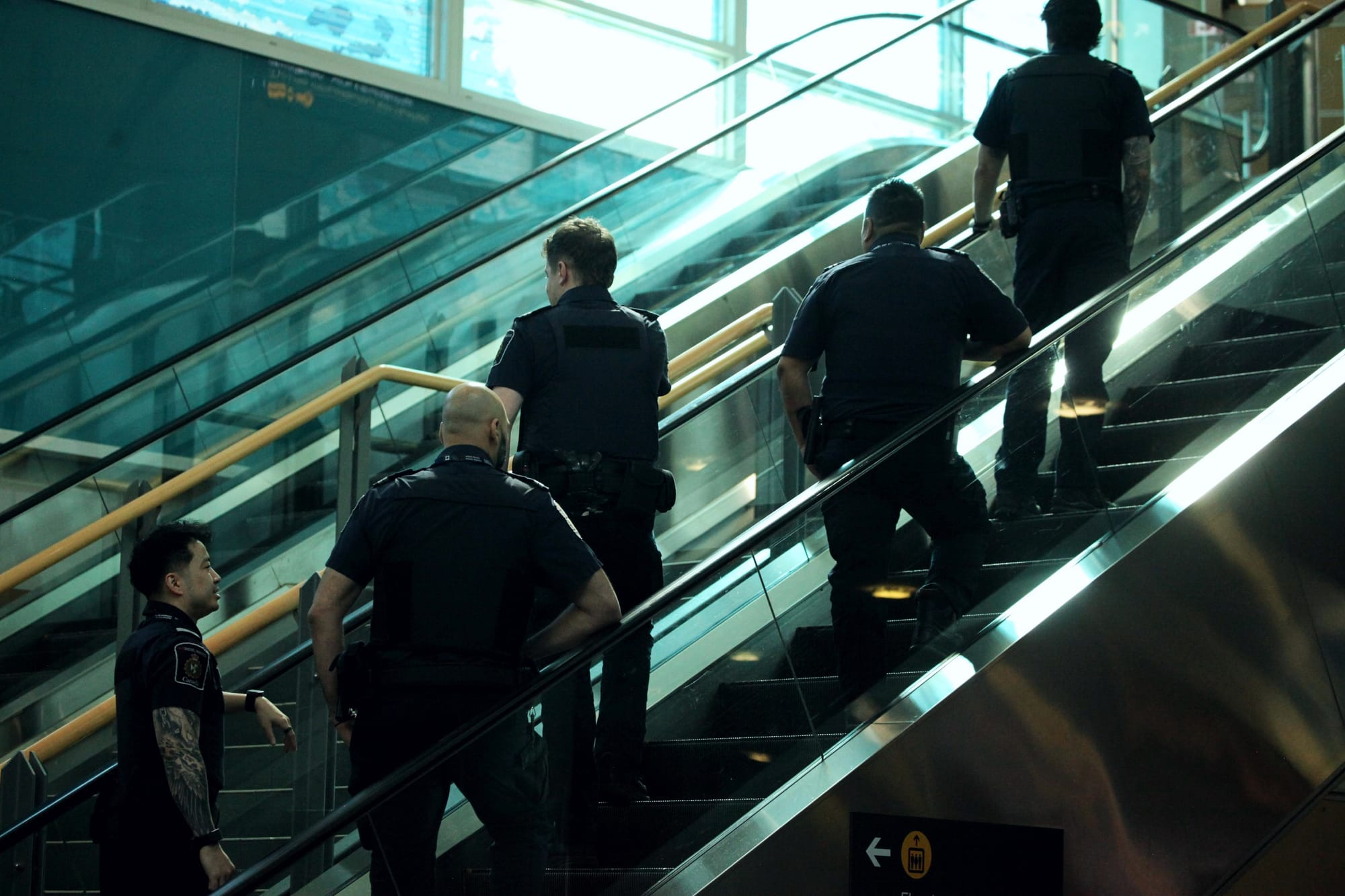 Five men in Canada Border Services Agency (CBSA) officer uniforms ride up an escalator