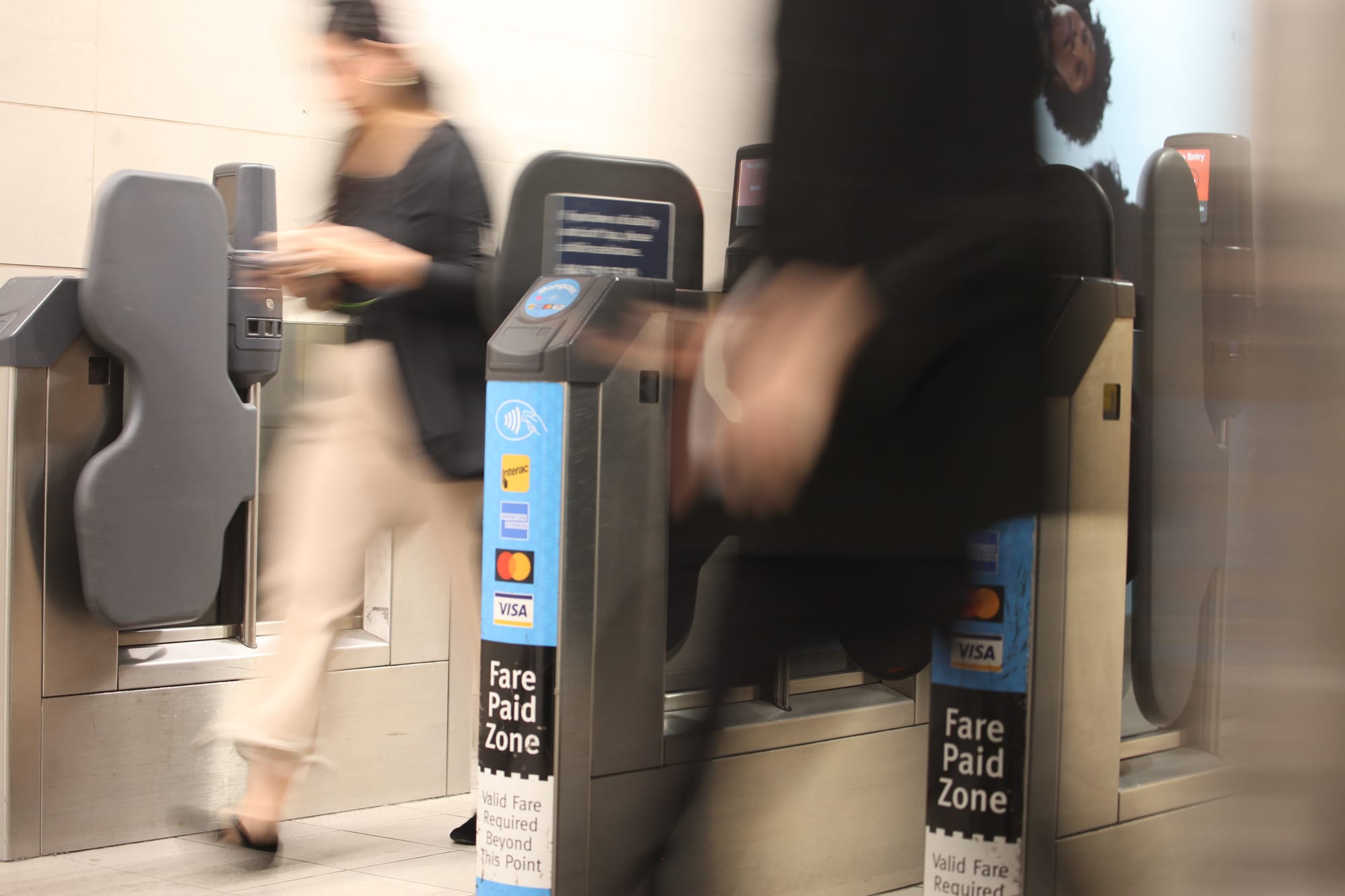 Two people are walking quickly through a gate at public transit station that reads, 'Fare Paid Zone'