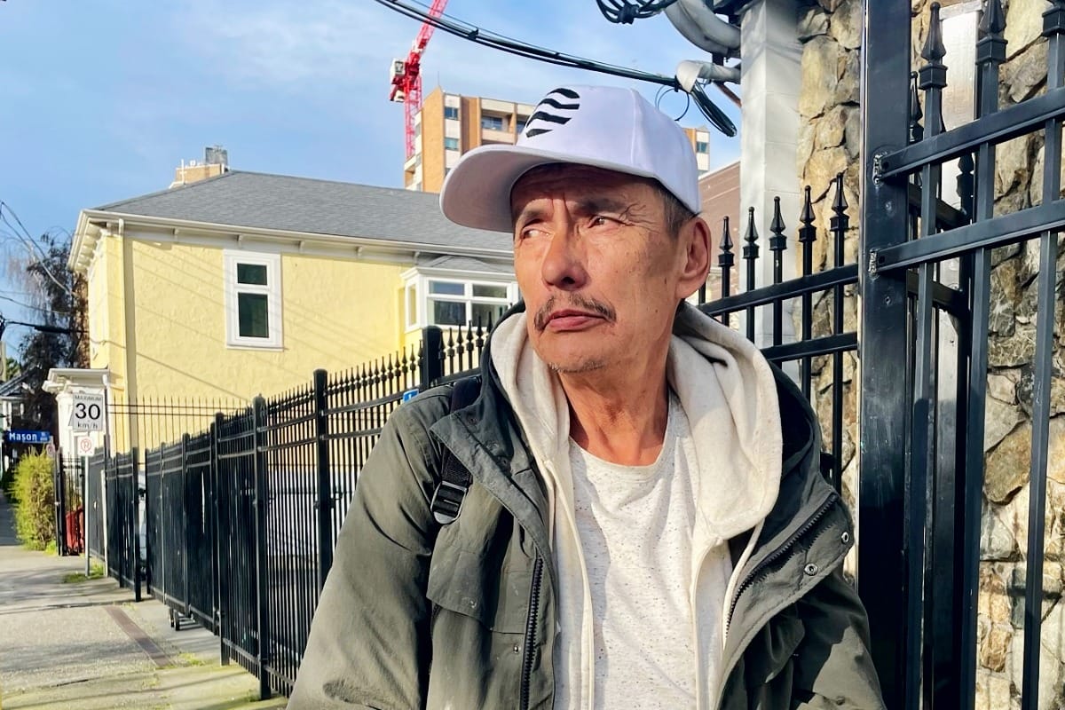 A man wears a hat and hoodie outside by a metal fence