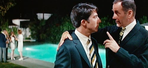 Still from The Graduate: by a lit swimming pool at night, Mr. McGuire (Walter Brooke) puts an arm around Benjamin (Dustin Hoffman) and raises one finger to make his point.