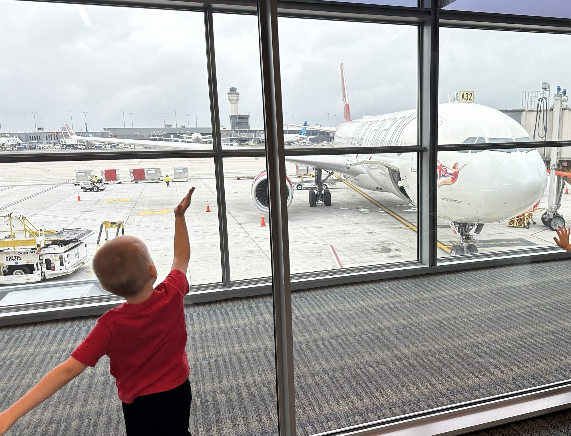 Toddler pointing at airplane through airport window while flying with kids