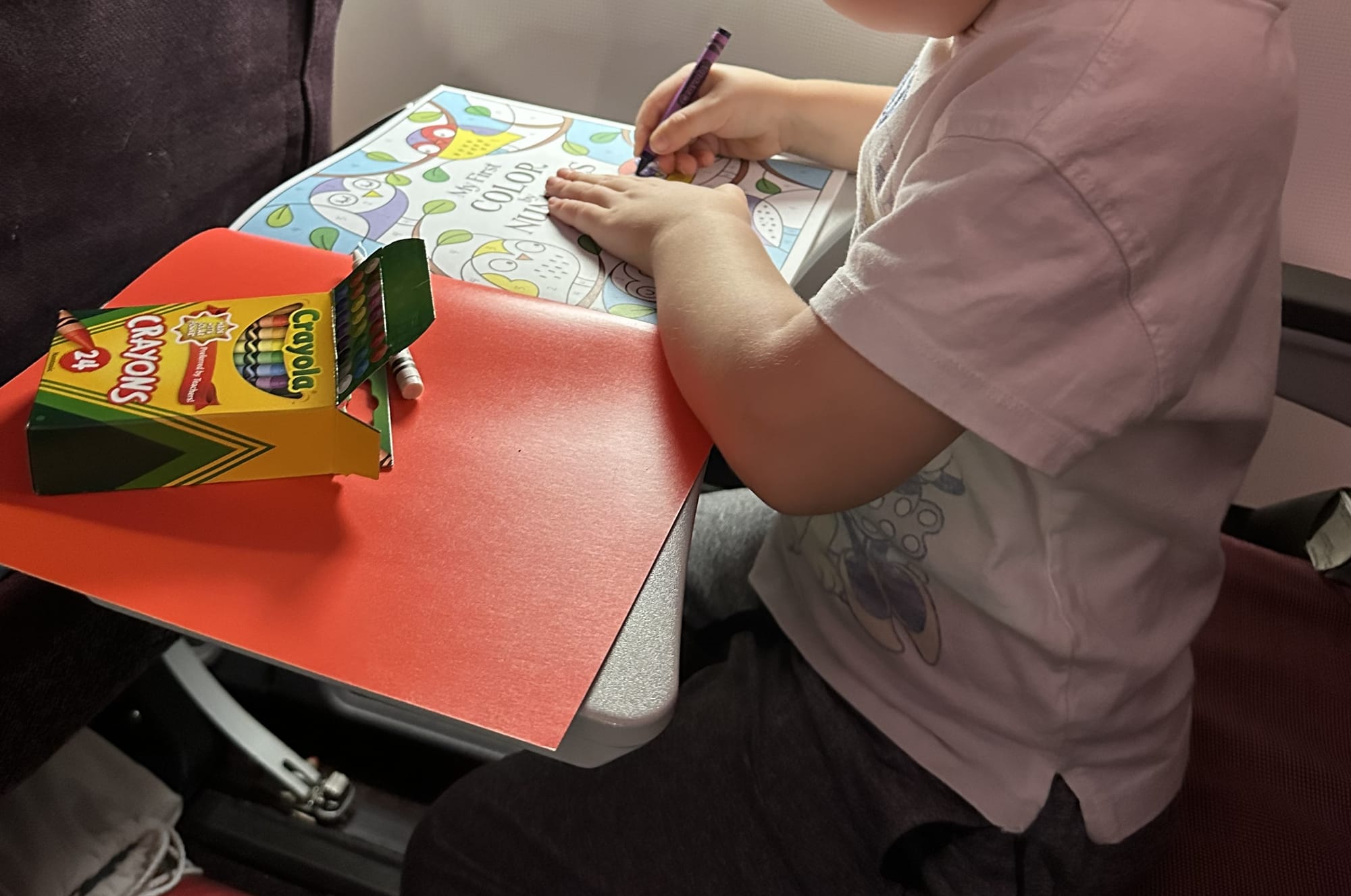 Young child coloring with Crayons on airplane tray table — activity ideas for flying with kids