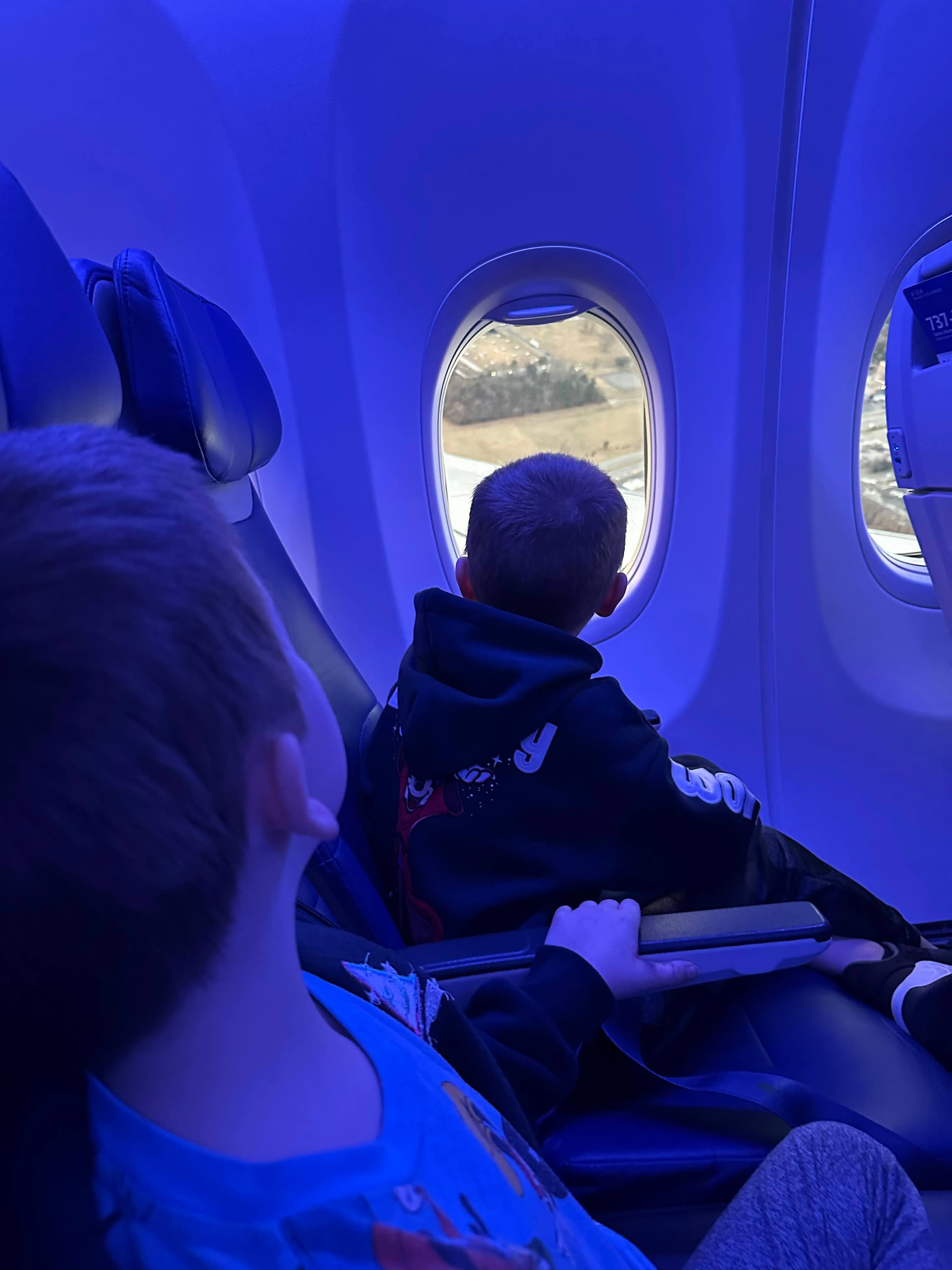 Two kids looking out airplane window with a tablet — screen-free and screen activities for flying with kids