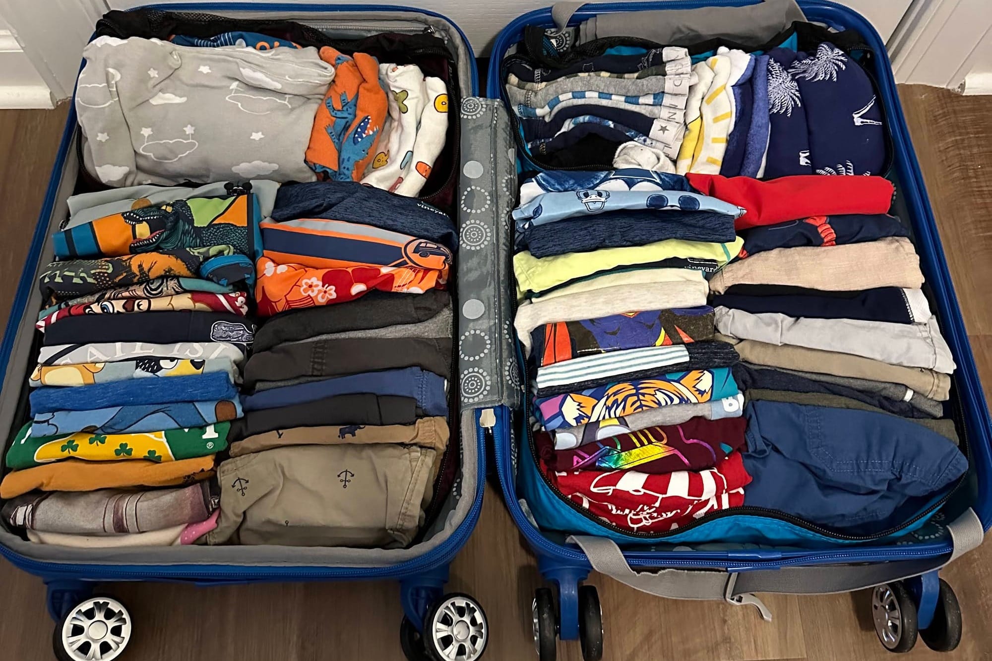A blue suitcase packed with rolled and folded kids' clothing, organized for a family road trip