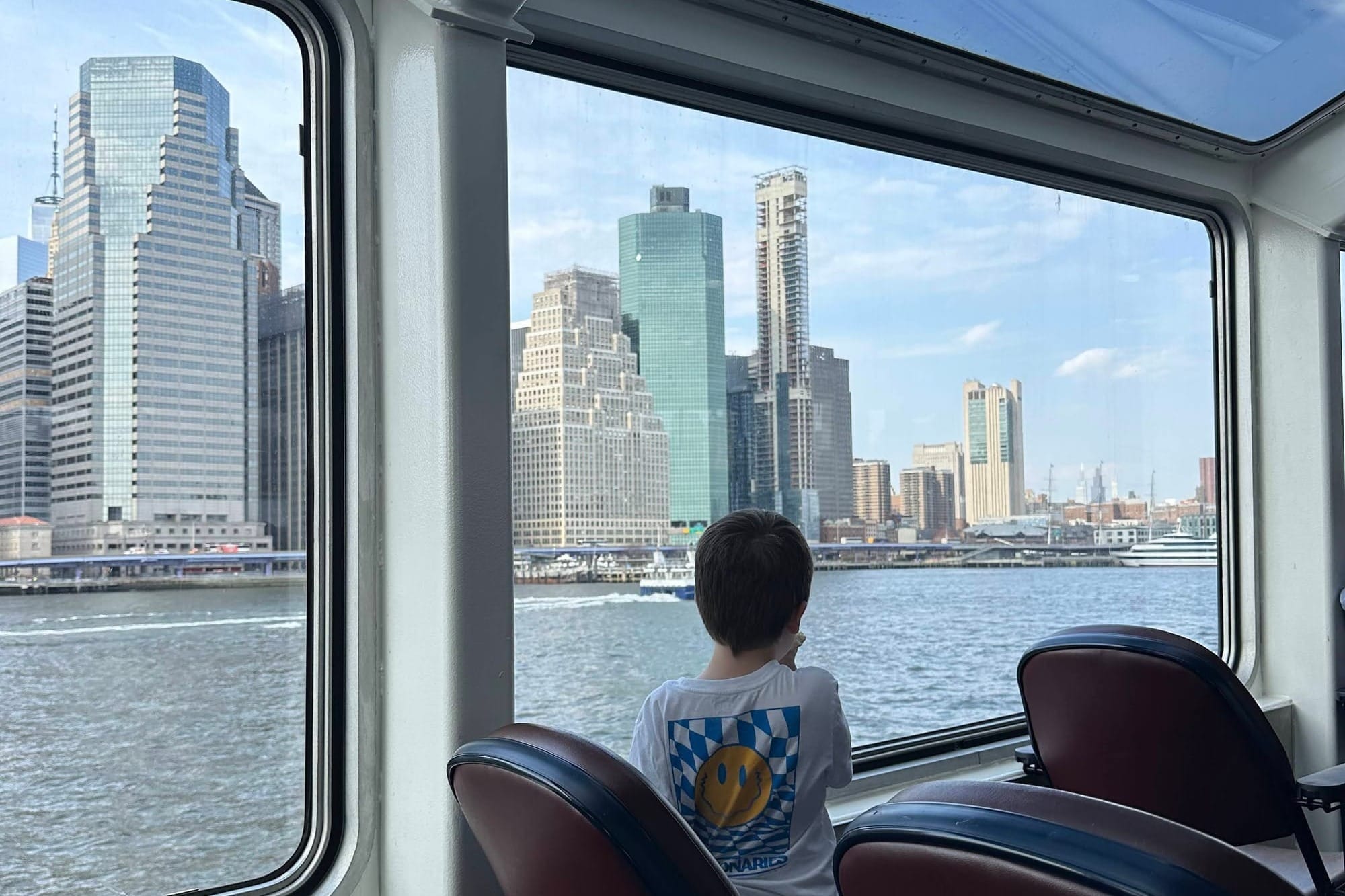 Child looking out boar window at NYC skyline, returning from a statue of liberty tour