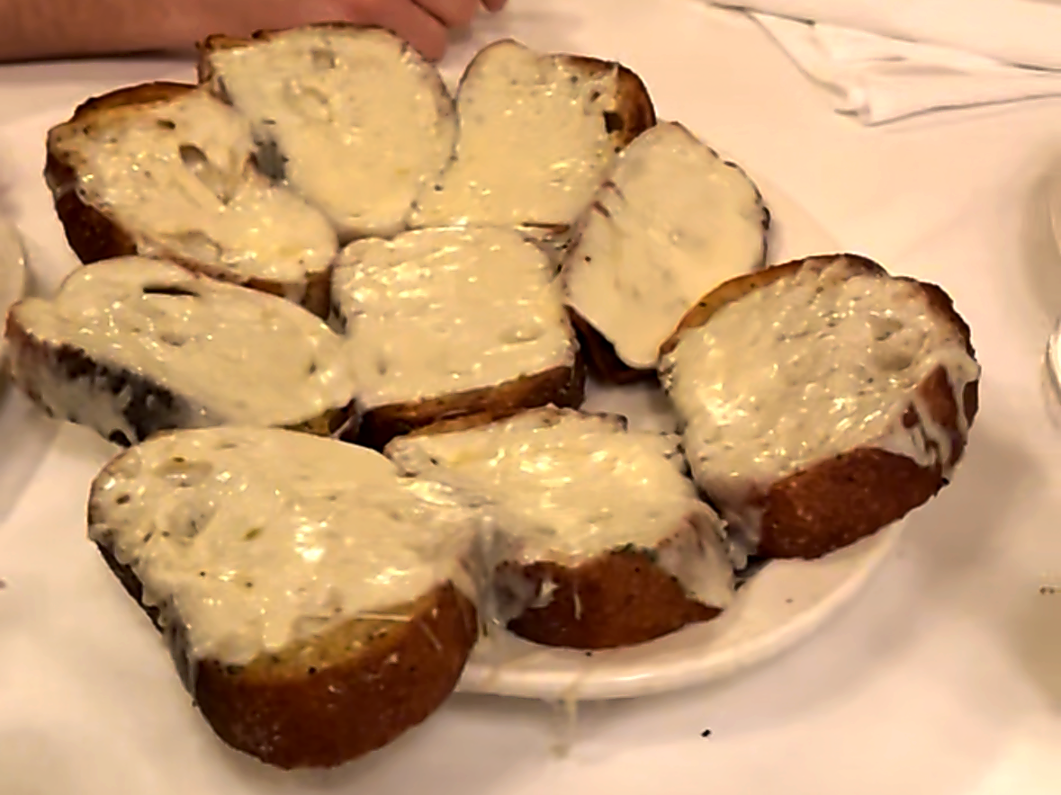 A slice of garlic cheese bread lifted from the plate with the cheese stretching, at Carmine's on the Upper West Side.