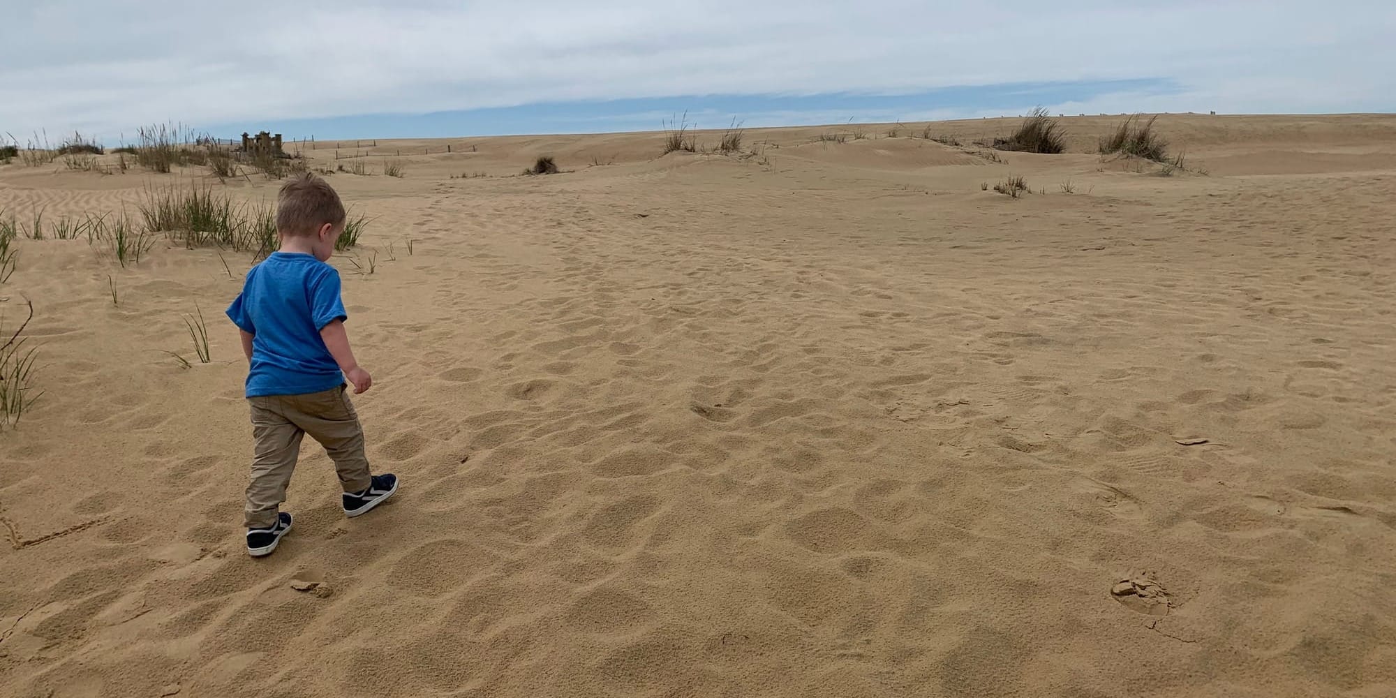 A young child in a blue shirt walks across vast sand dunes at Jockey's Ridge State Park in Outer Banks, NC.