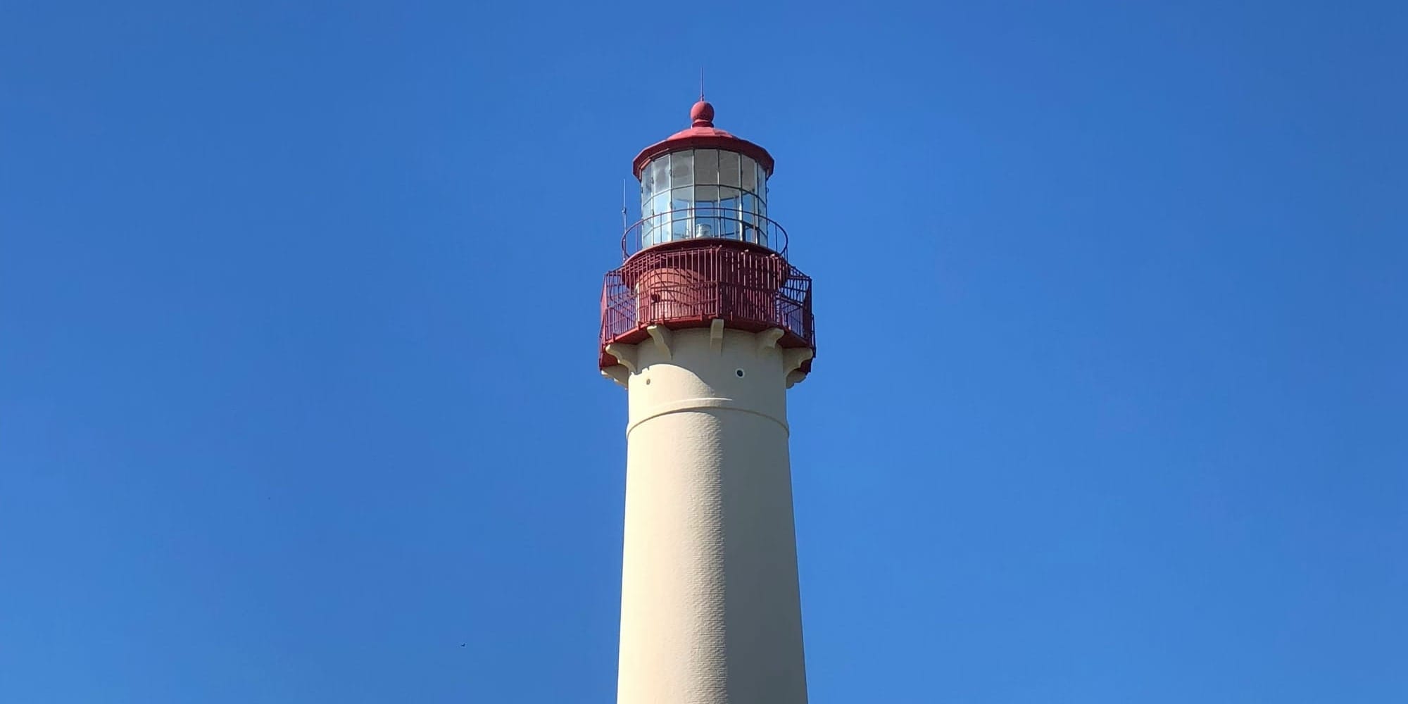 The Cape May Lighthouse, a tall white tower with a red top, against a clear blue sky.