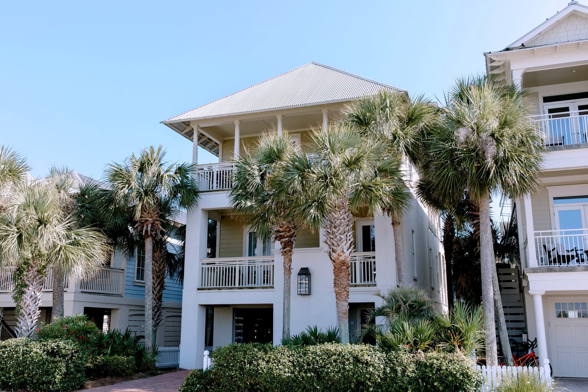 Three story beach rental home with wraparound balconies shaded by tall palm trees, ideal for a multigenerational family group