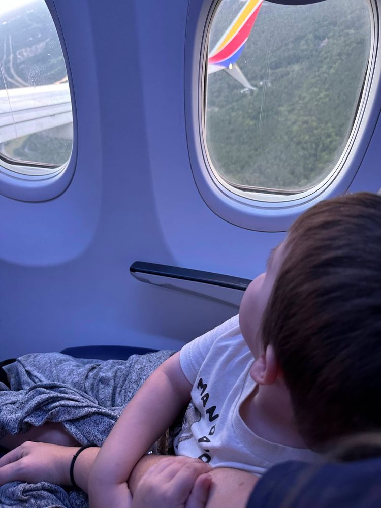 Child resting on parent's lap looking out Southwest Airlines window — flying with young kids tips