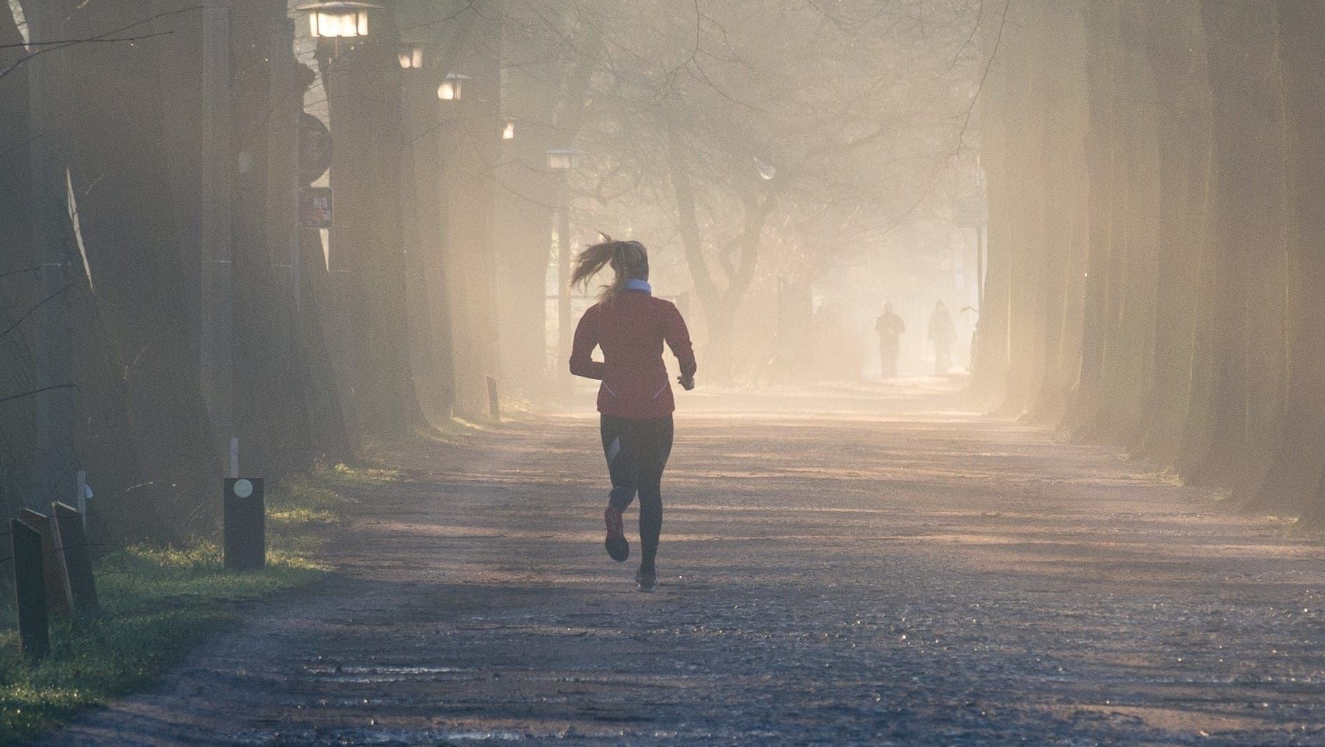 Morning jogger running through a misty tree-lined path, surrounded by soft sunlight.