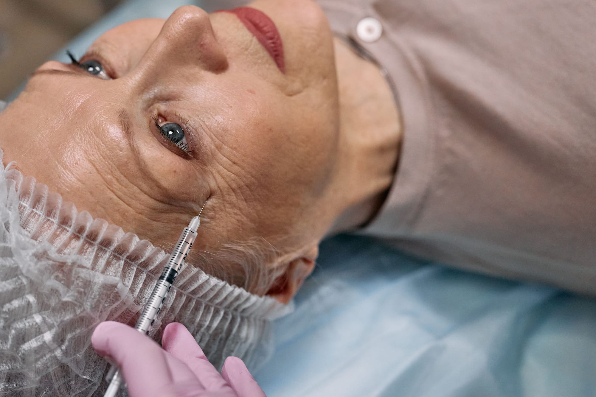 Older woman receiving a cosmetic injection near her eye.