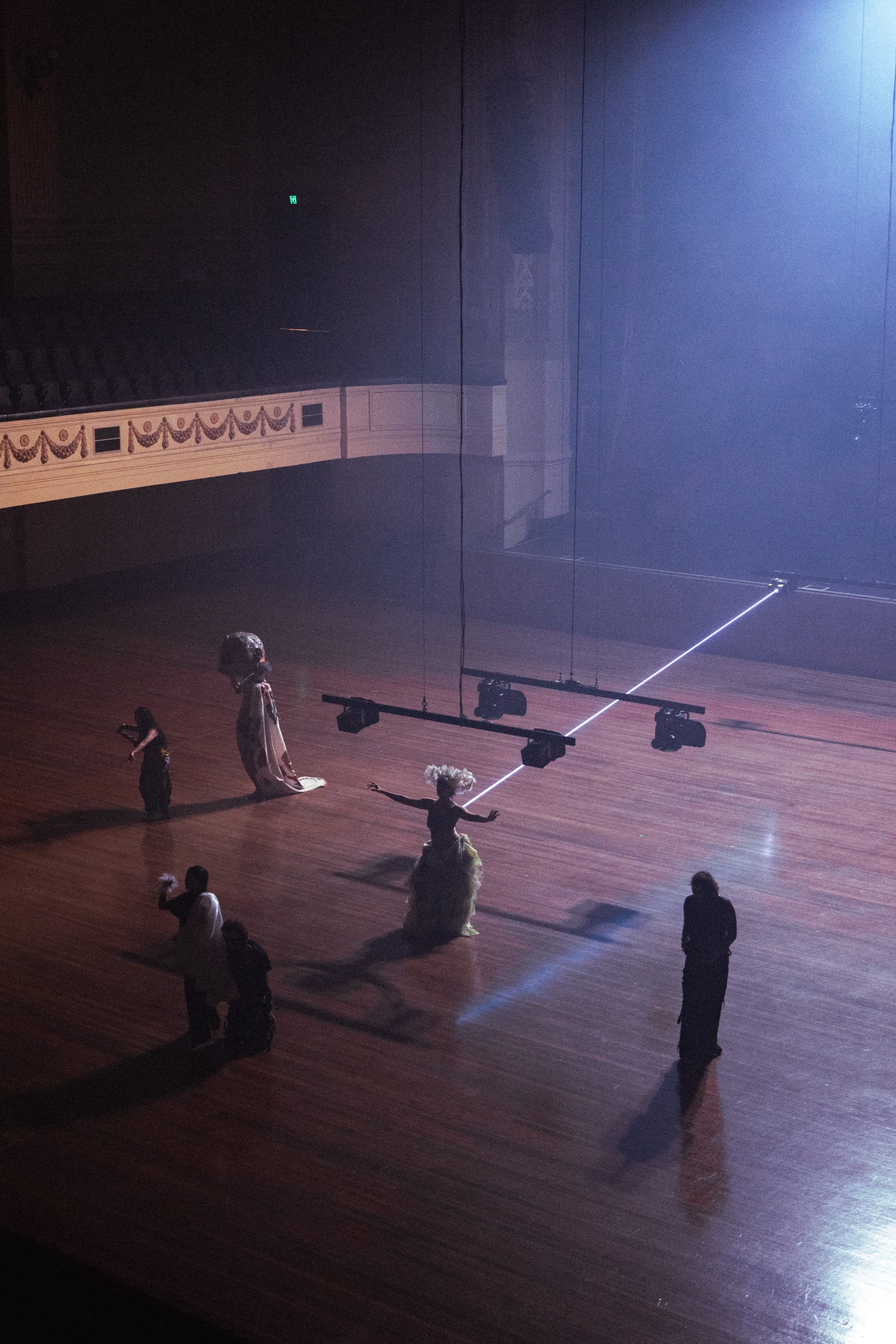 Six performers are dispersed across the vast timber floor of Melbourne Town Hall beneath suspended lighting equipment, with a single bright laser beam cutting diagonally through the space in Chunky Move’s Time Remaining.