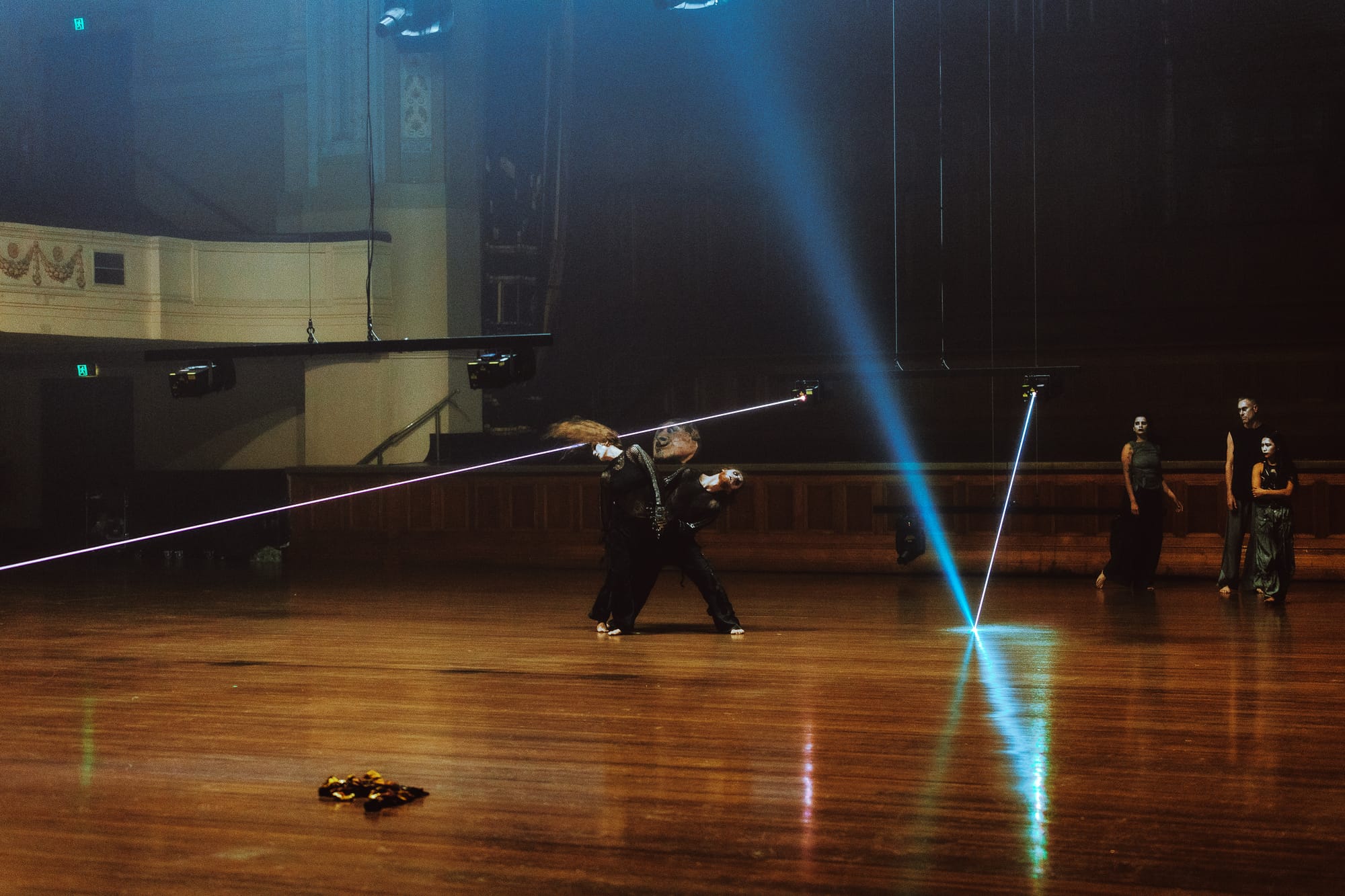 Performers move across the vast timber floor of Melbourne Town Hall as blue and violet laser beams cut through the space between them in Chunky Move’s Time Remaining.