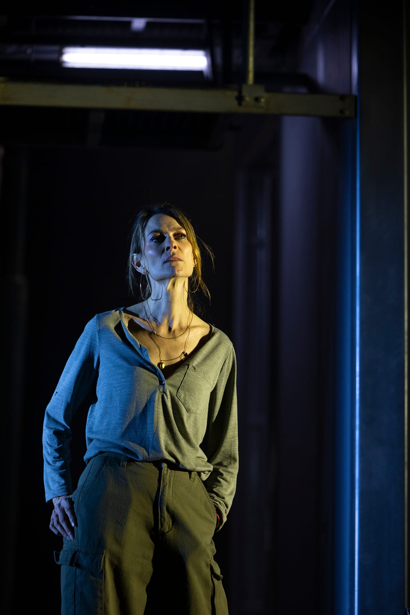Pamela stands alone in a narrow wash of blue light, surrounded by darkness on the stage.
