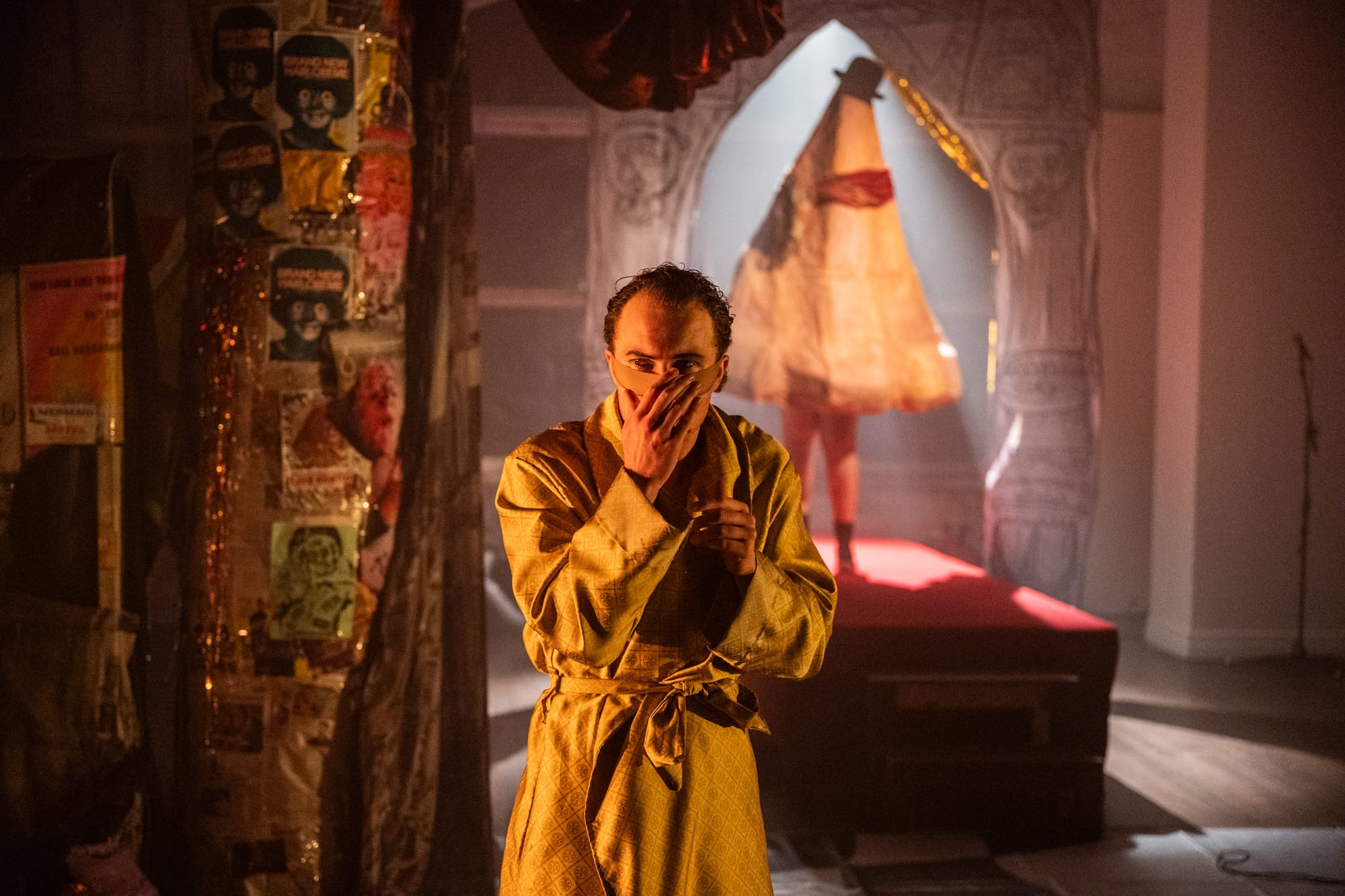 Cooper Donald McDonald as Major Pepsi covers his noseless face with one hand while an enormous sculpted nose looms behind him on the dimly lit stage.