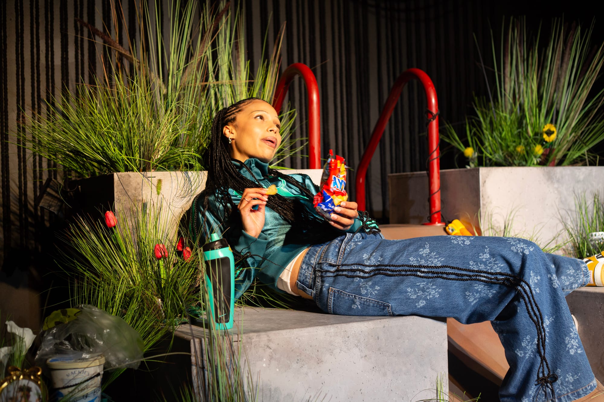 Lucy Ansell reclines among concrete platforms and flowers under warm stage lighting in Funeral Flowers.