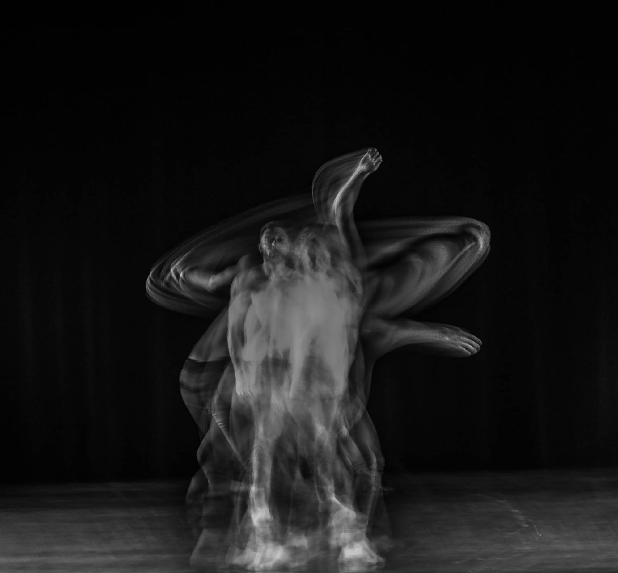 A black-and-white long-exposure photograph of a dancer, their body and sweeping arms appearing in multiple overlapping positions.