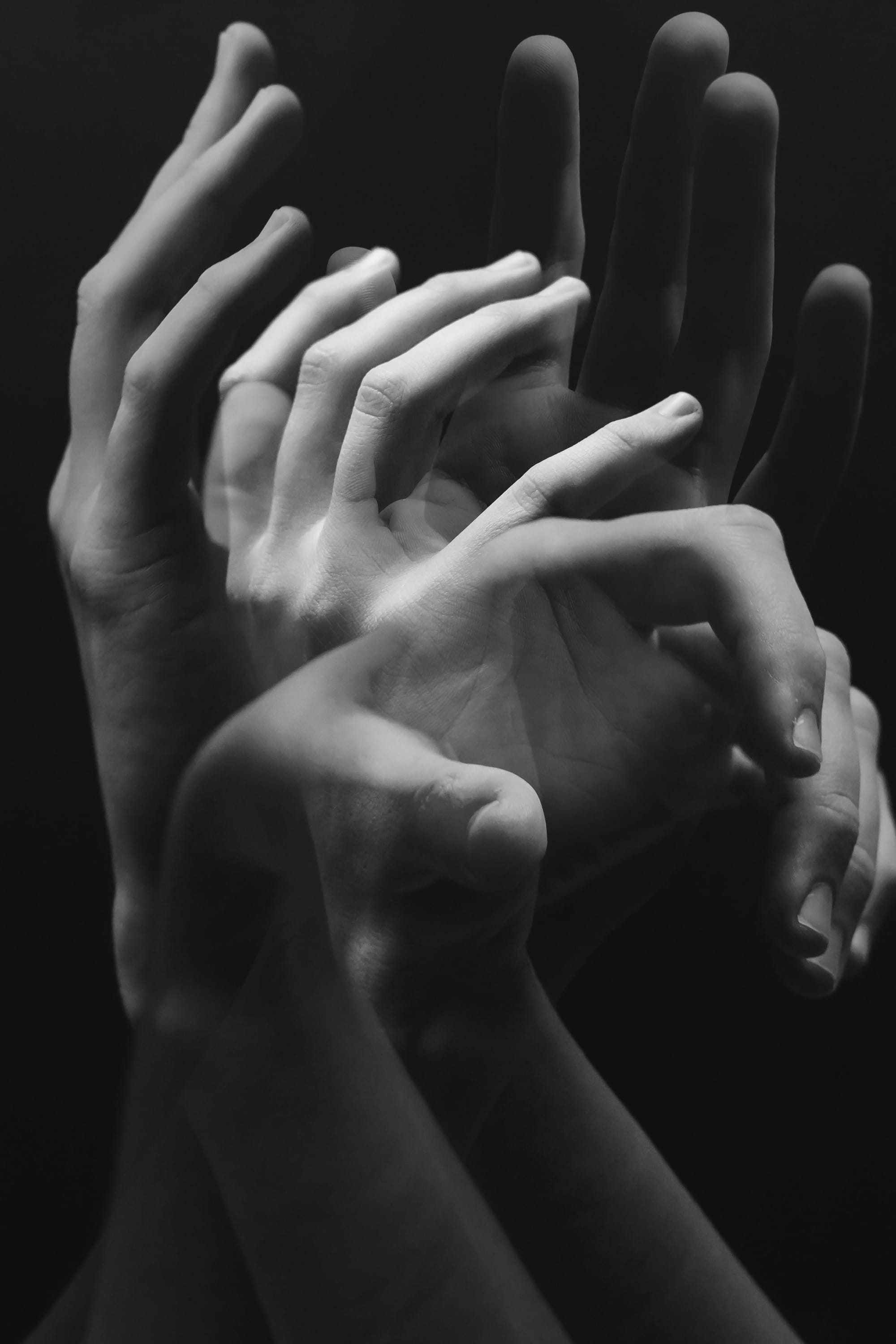 Black-and-white multiple-exposure photograph of hands and arms overlapping in a series of reaching gestures.