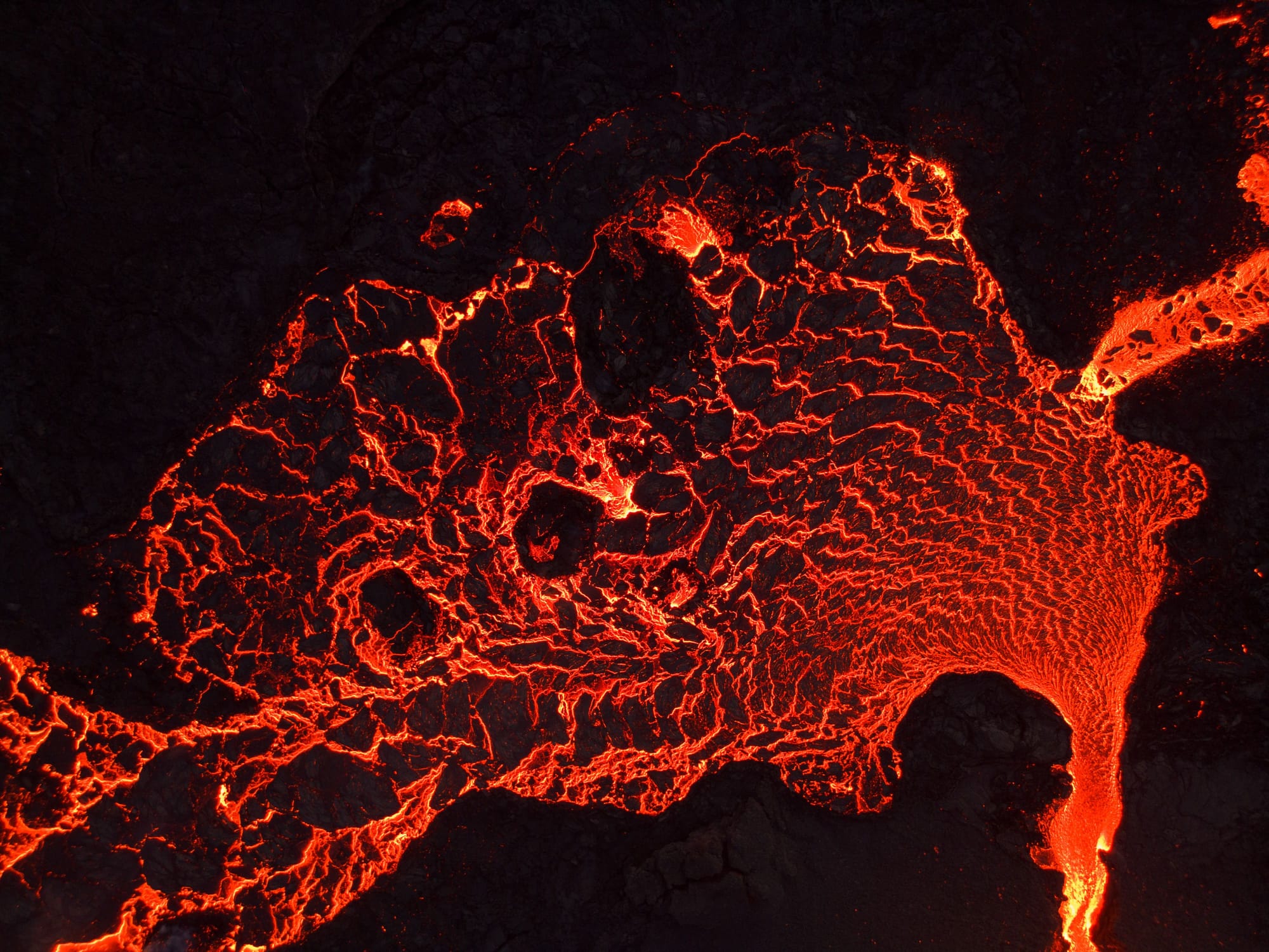 Glowing orange lava flowing through cracks in a dark volcanic surface in Iceland.