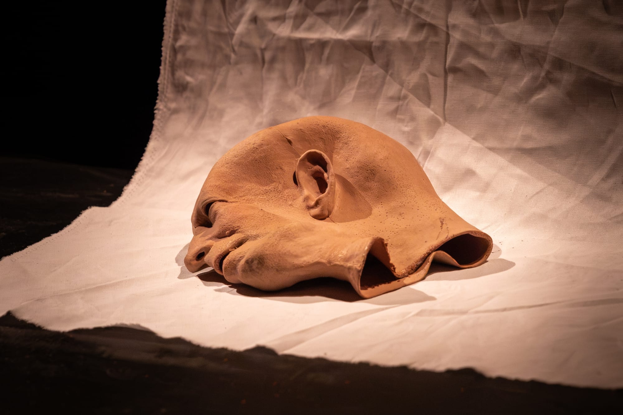 A flesh-coloured theatrical mask lies on white fabric under a spotlight in Cold War 2.0.