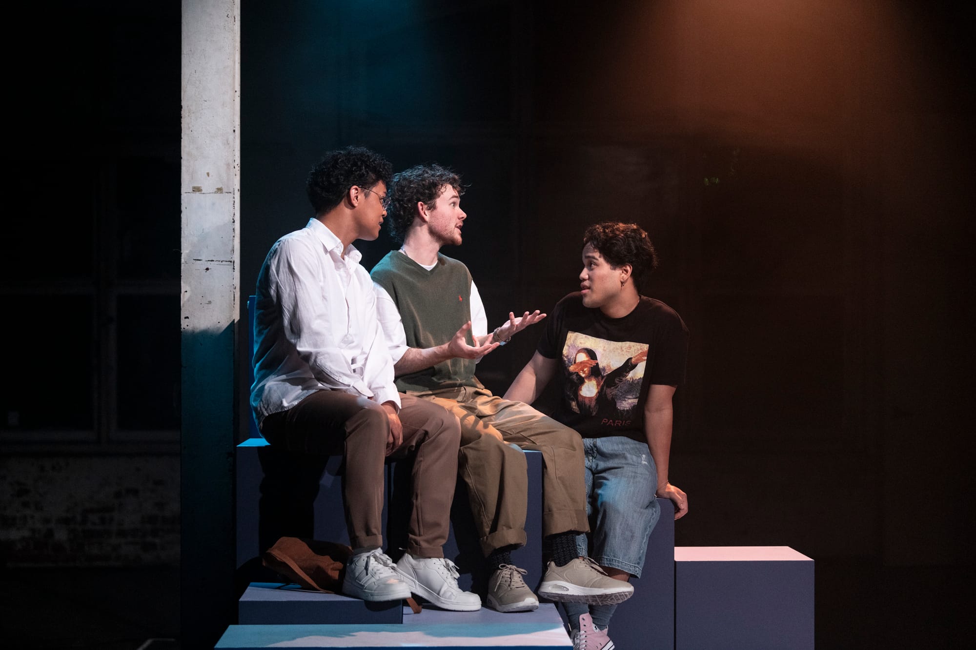 Chad Rosete, Lawrence Hawkins and Ken Paolo sit together on blue blocks onstage, Hawkins gesturing as the three appear to be in animated conversation.