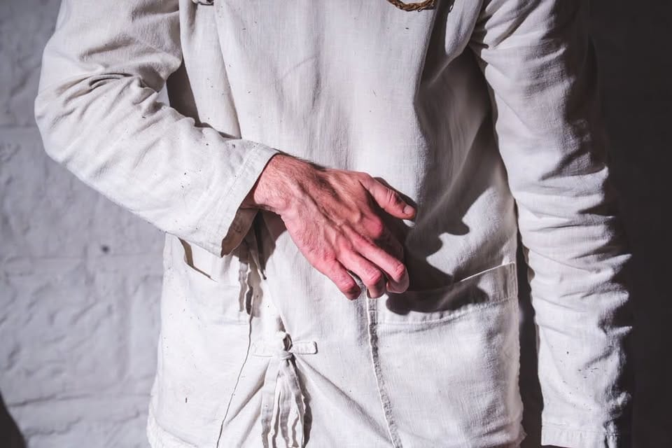 Close view of Luke Casserly dressed in white, one hand resting across his abdomen during Distillation.