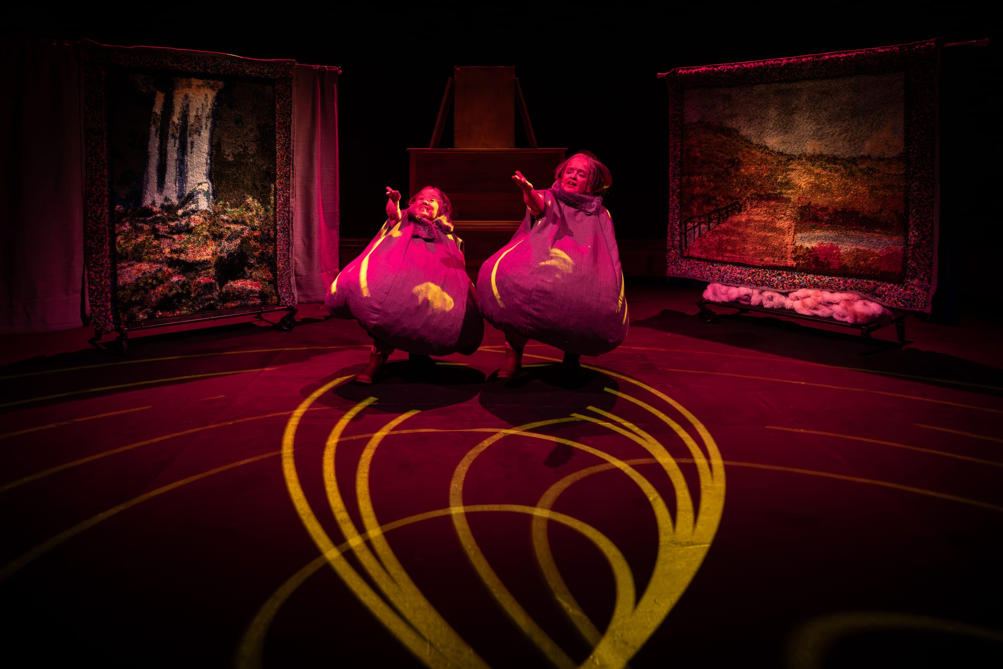 Hawkins and Prowd dance inside enormous grey beanbag costumes under vivid stage lighting, with woolly landscape hangings behind them.