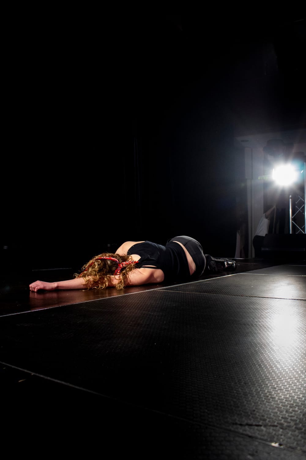Oriana Morris-Johnson as Grant Smith lies face-down and motionless on the dark stage, one arm extended, after the play’s final confrontation.