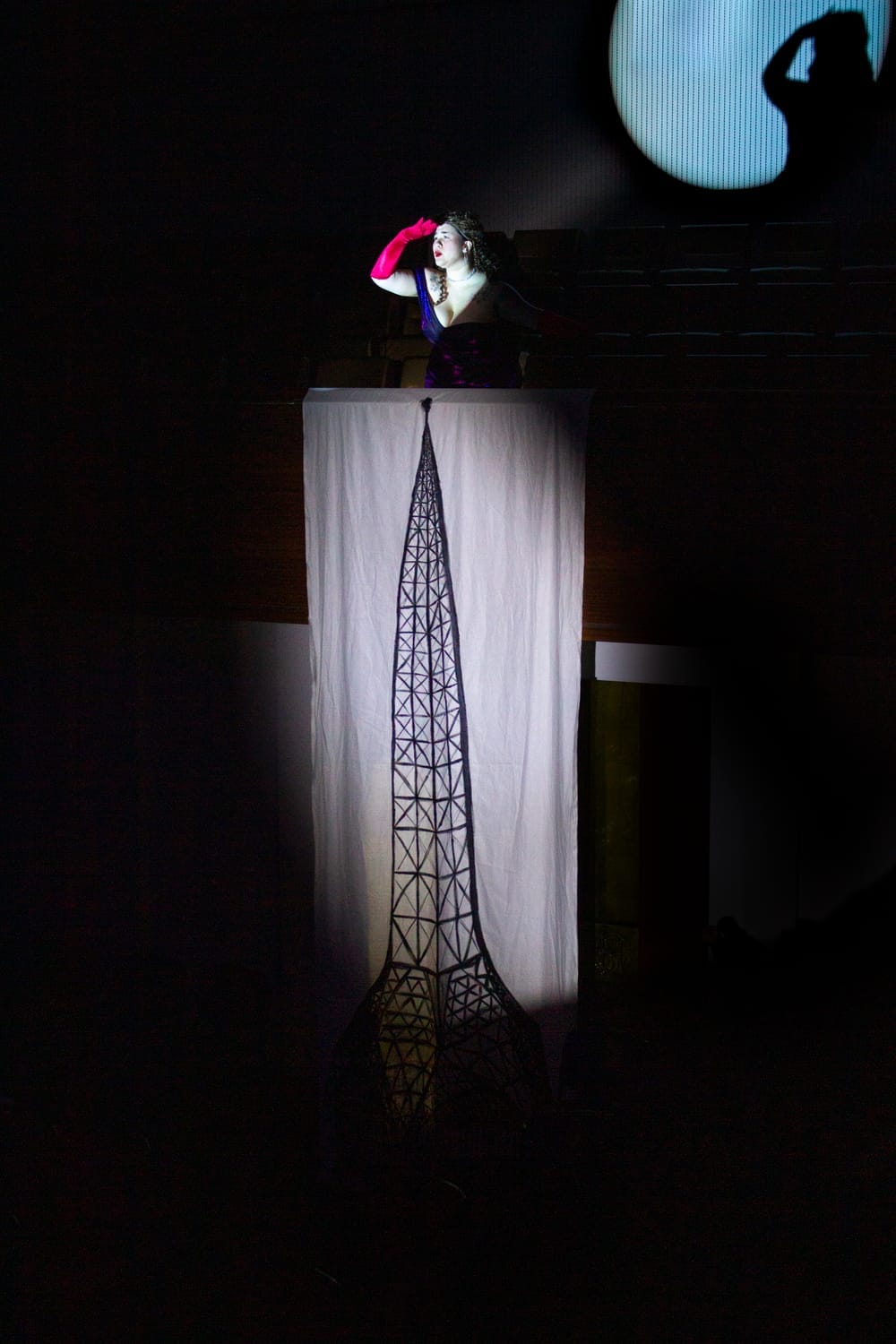 Mon Wing-Yun as Philanthropy Philharmonica peers into the distance from the balcony above a handmade depiction of the Arts Centre Melbourne spire.