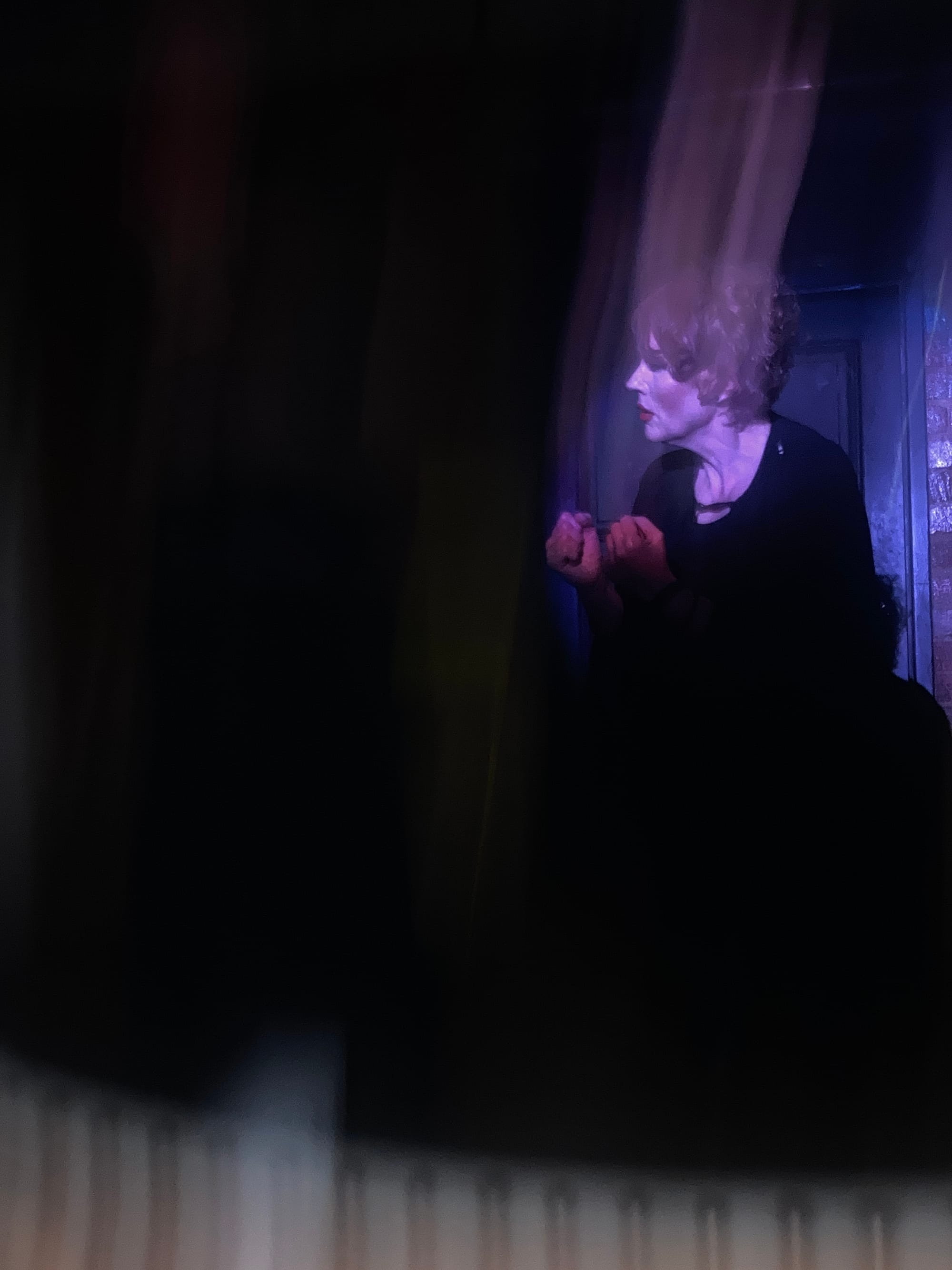 Rebecca Howell (Character 2) in Hitherto, framed by the doorway and atmospheric stage lighting.