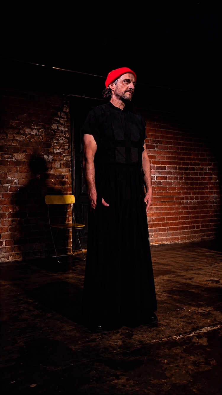 Arthur Angel (Character 1) onstage in Hitherto, wearing the character’s red beanie and black costume.