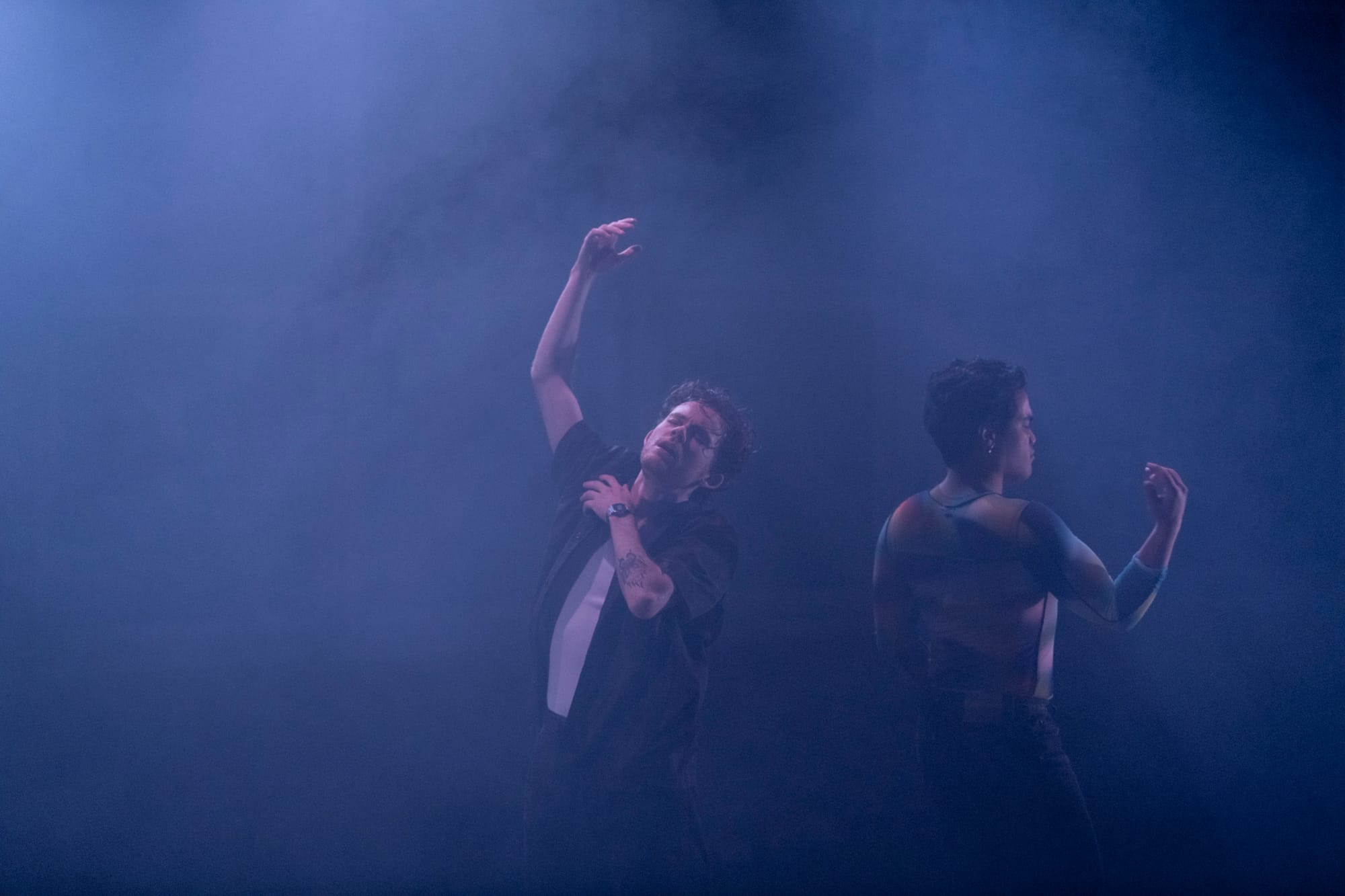 Lawrence Hawkins and Ken Paolo dance back-to-back in a haze of blue stage light, each with one arm raised in a loose dance movement.