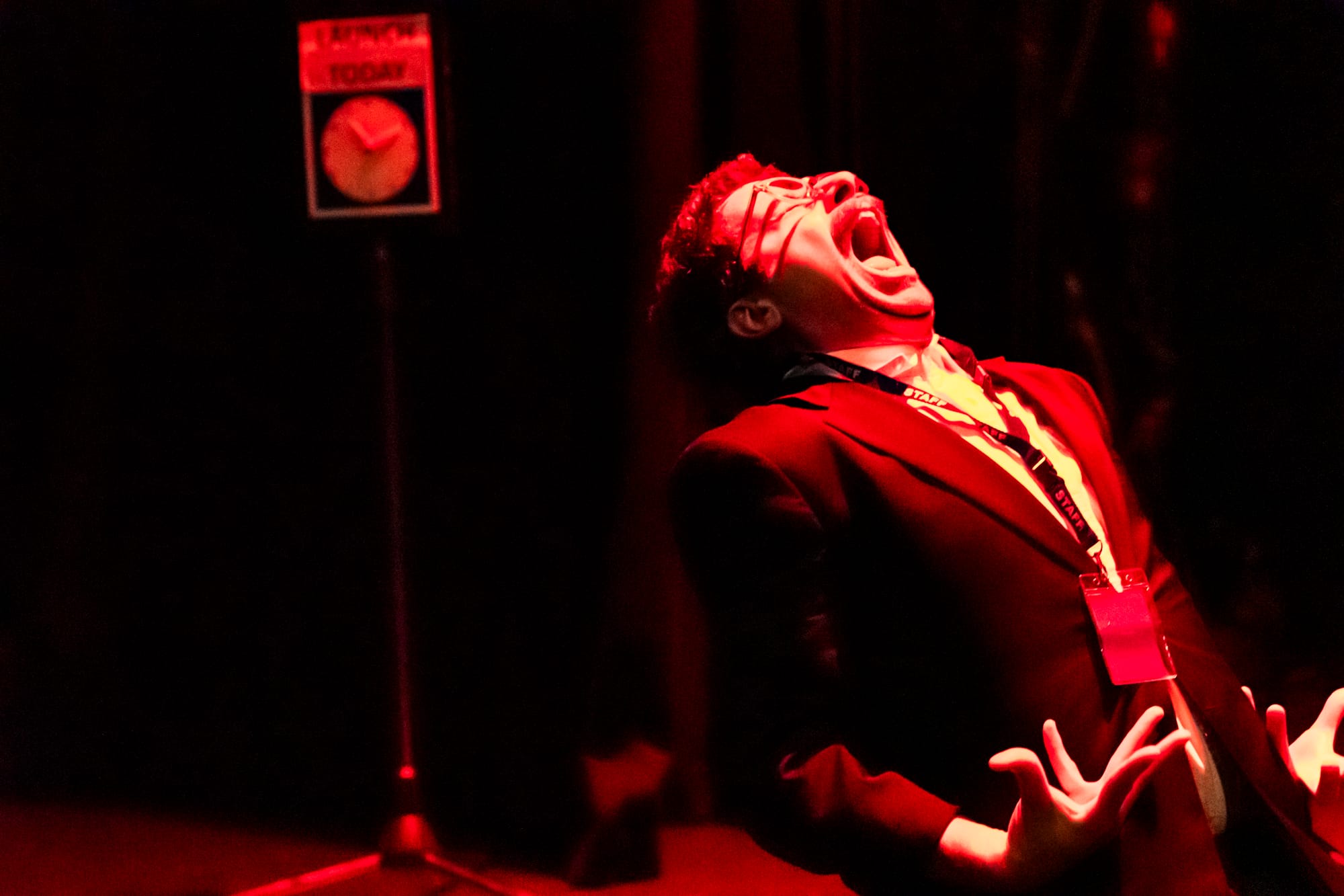 Tim Sneddon throws his head back and opens his mouth in a silent scream, hands spread beside him as the stage is flooded with intense red light.