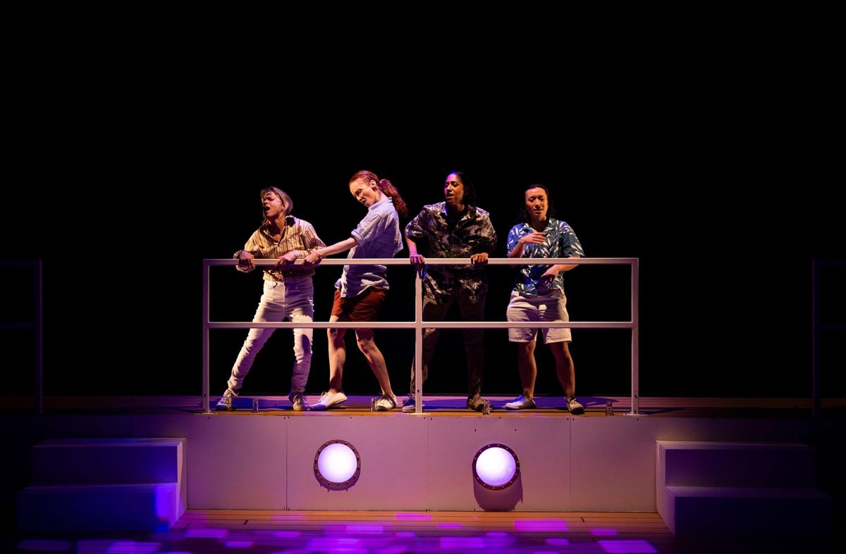 Four performers dance along the upper deck of a cruise ship under purple and blue nightclub lighting.