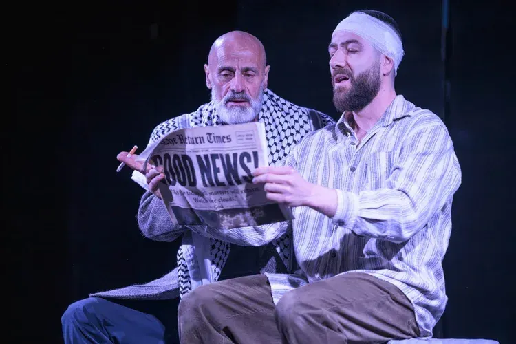 Rashid Taki as Marwan, wearing a keffiyeh, sits beside Mohammed El Kesm as The Man, whose head is bandaged, as they read a newspaper together in The Return.