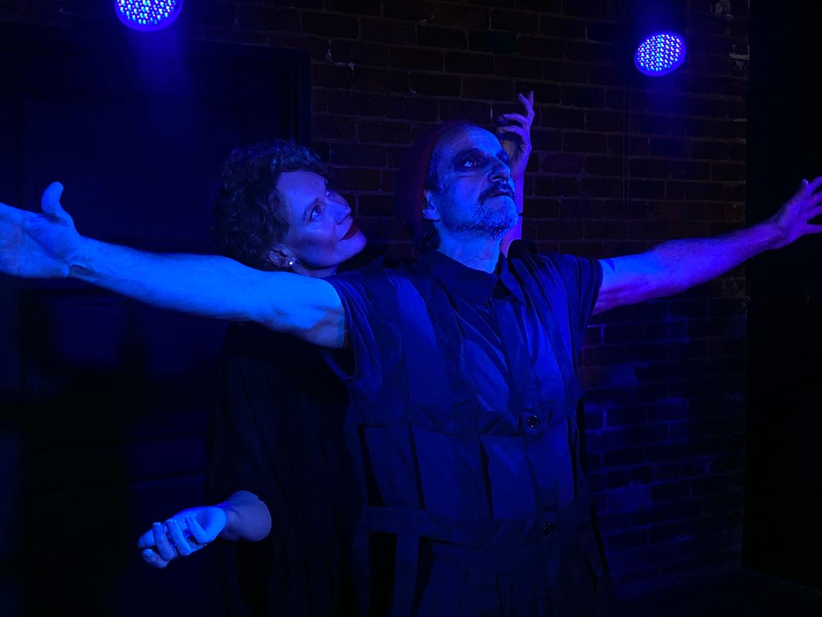 Arthur Angel (Character 1) and Rebecca Howell (Character 2) in Hitherto, arms outstretched under saturated blue stage lighting