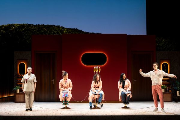 Five performers on the Losing Face set, with three women seated in treatment chairs between a nurse and wellness guru.